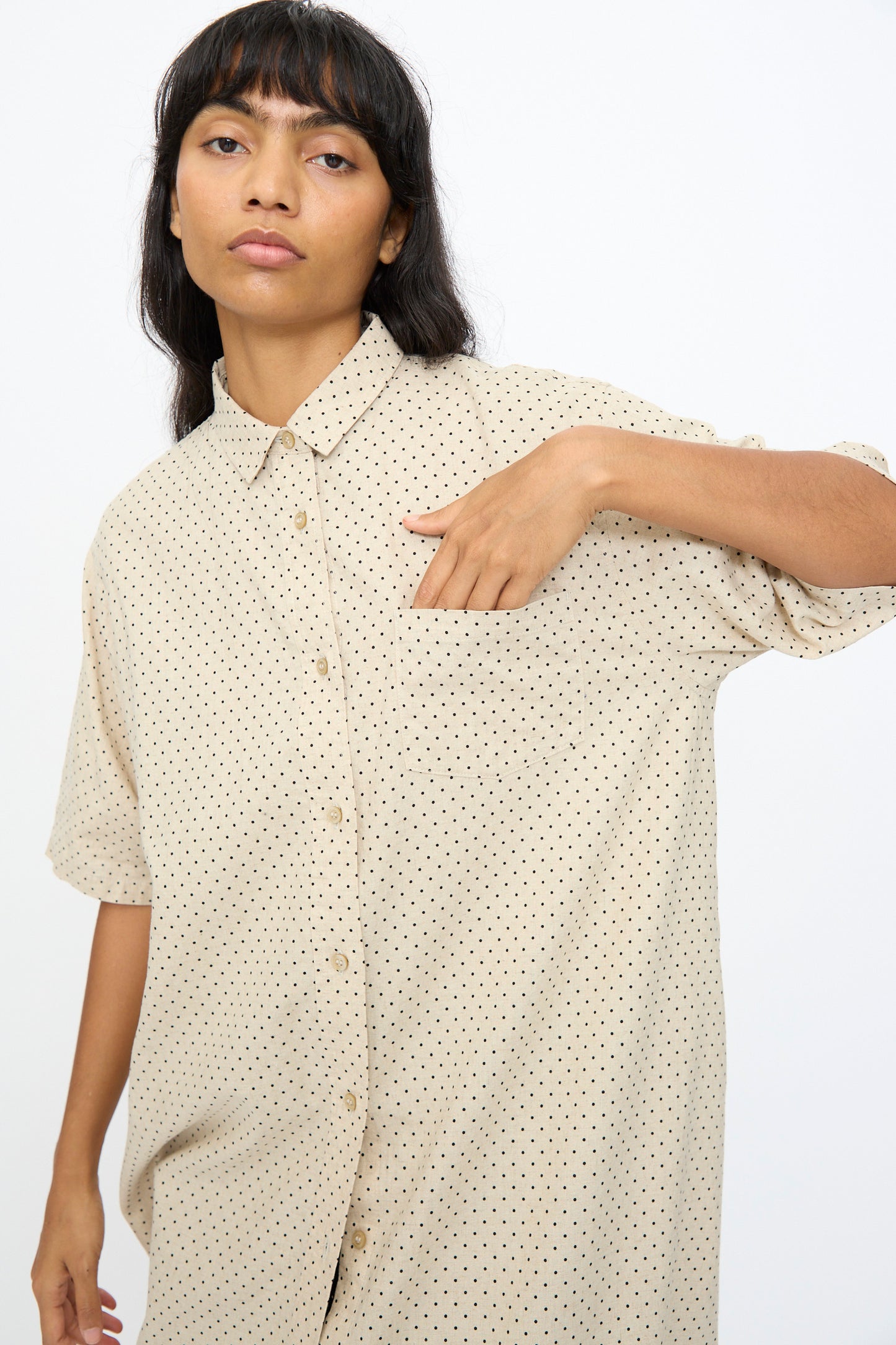 A woman wearing the Ichi Antiquités Cotton Linen Dot Dress in Natural, featuring black polka dots and a chest pocket, stands against a plain background with one hand inside the pocket.