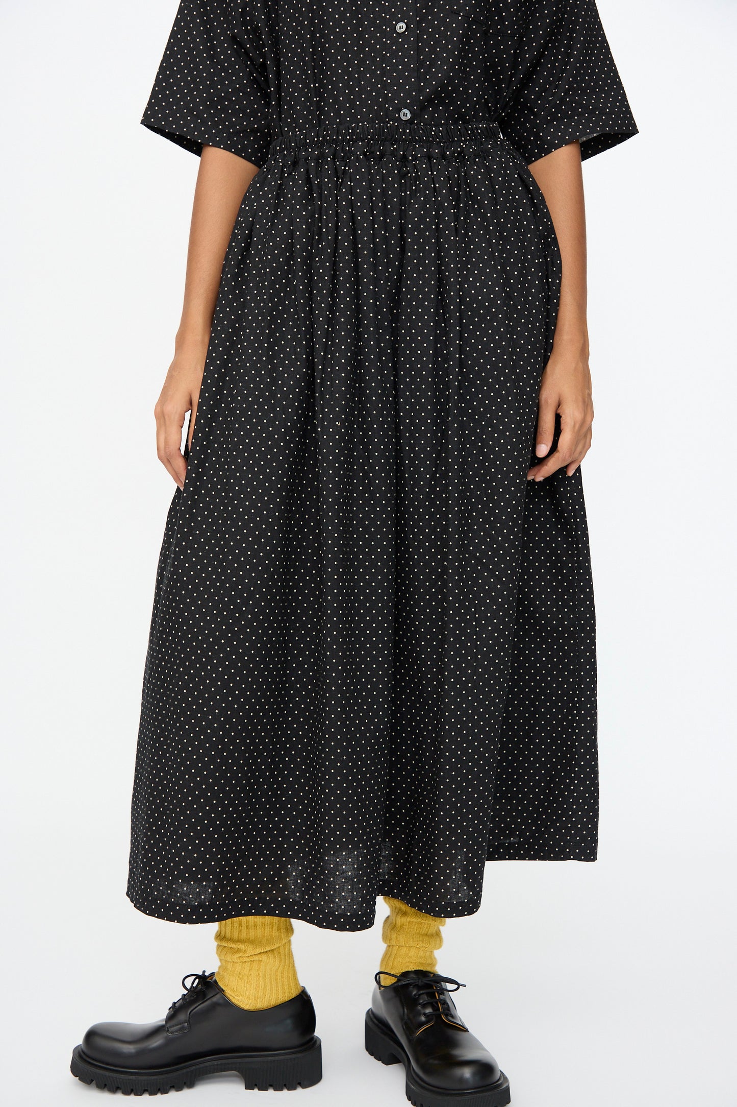 Someone stands against a plain white background wearing the Ichi Antiquités Cotton Linen Dot Skirt in Black, paired with yellow socks and black platform shoes.