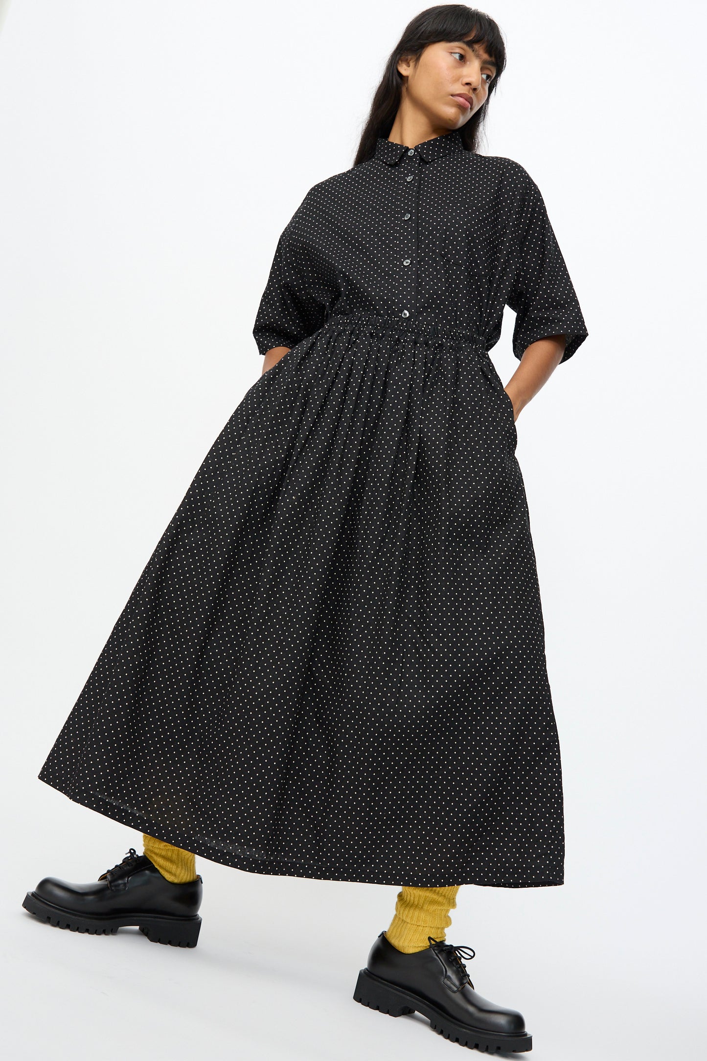 A woman wearing the Ichi Antiquités Cotton Linen Dot Skirt in Black with black chunky shoes and yellow socks stands against a plain white background.