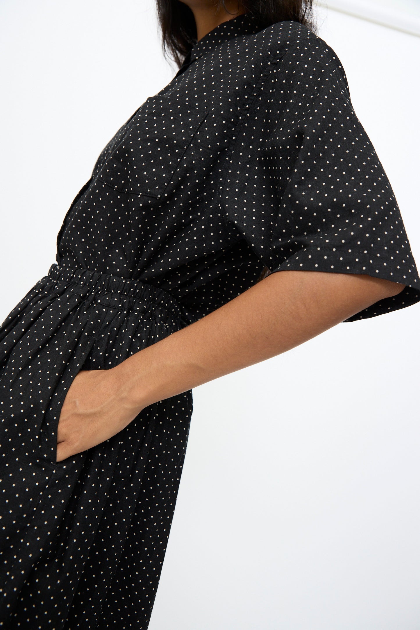 Wearing the Ichi Antiquités Cotton Linen Dot Skirt in Black, featuring white polka dots, a person poses with one hand in their pocket against a plain background.