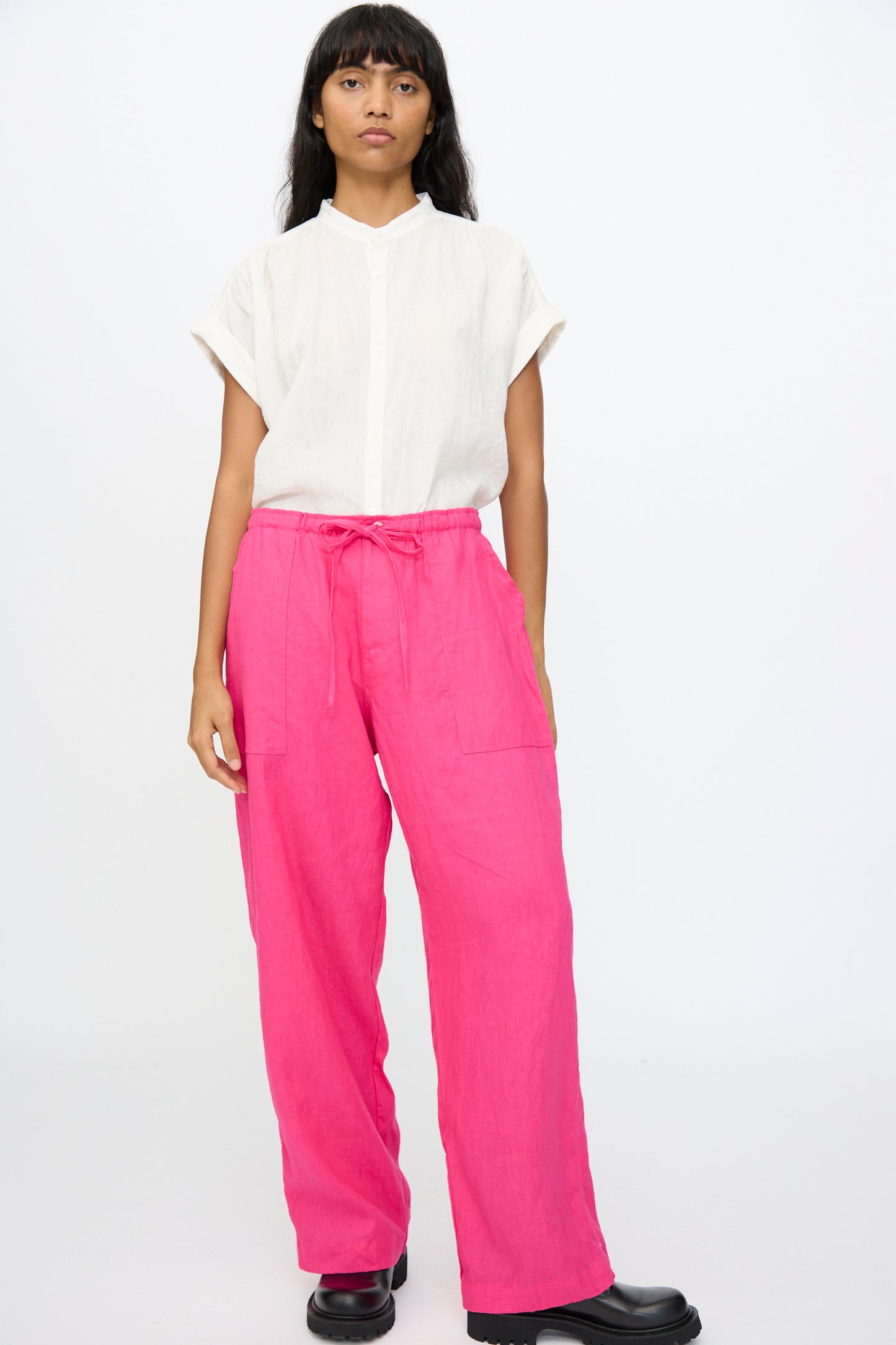 A person stands against a plain background wearing a white short-sleeve shirt, black shoes, and Ichi Antiquités Color Linen Pants in Pink—relaxed fit with pockets, made in Japan.