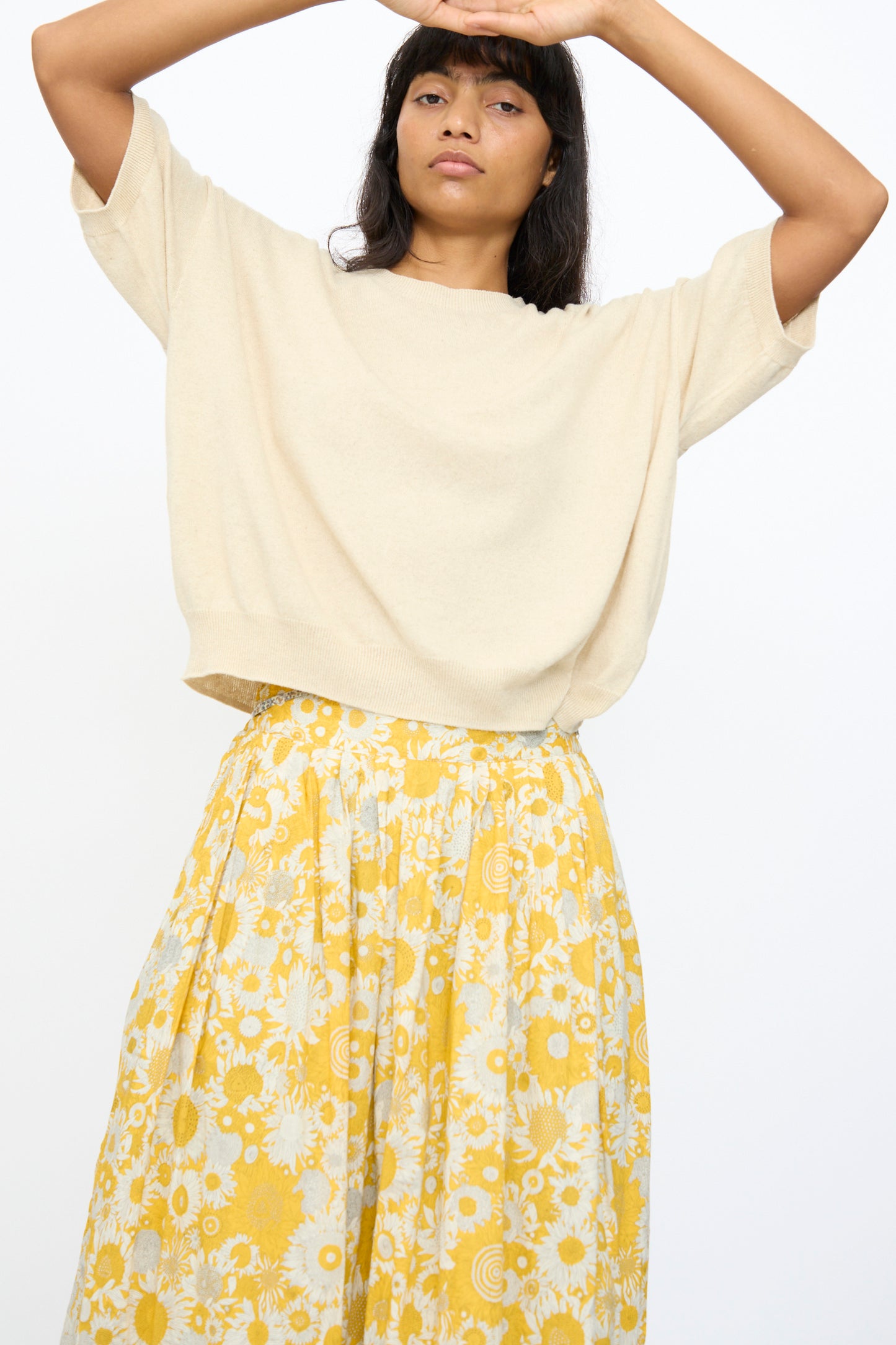 A woman wears the Ichi Antiquités Cotton Linen Pullover in Natural with a yellow floral skirt, standing against a plain white background with her arms raised overhead.