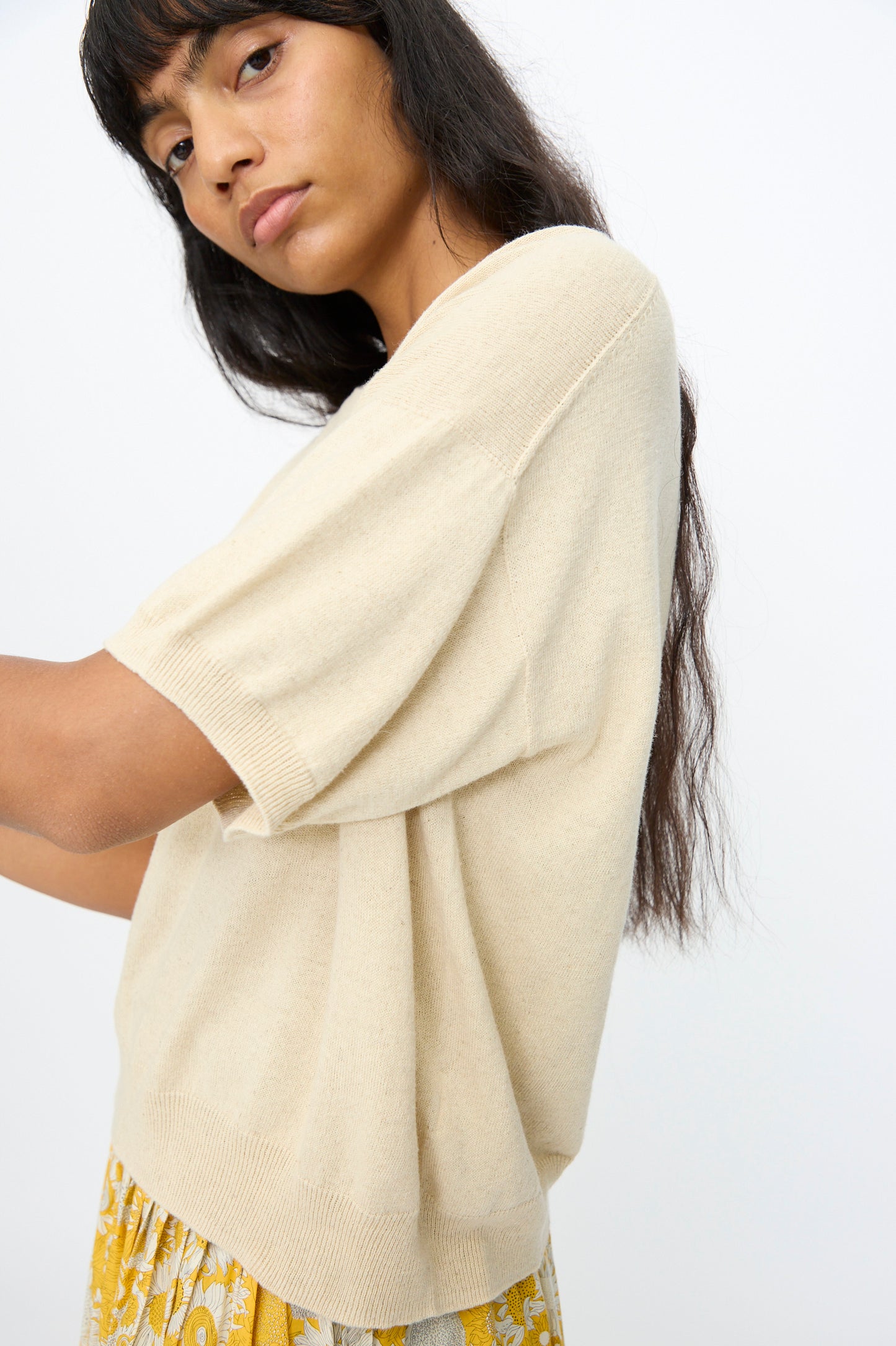 A woman with long dark hair wears the Ichi Antiquités Cotton Linen Pullover in Natural with a yellow patterned skirt, standing against a plain light background.