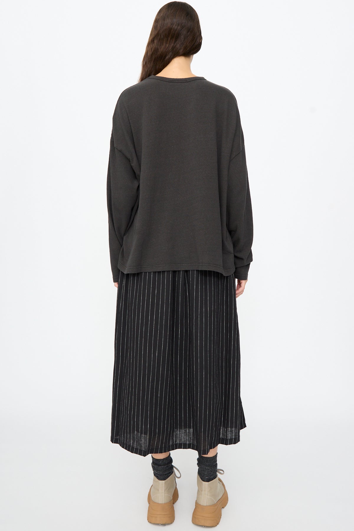 A person viewed from behind wearing a black Ichi Antiquités Cotton Loose Pullover, a black pinstriped midi skirt, dark gray socks, and tan sneakers.