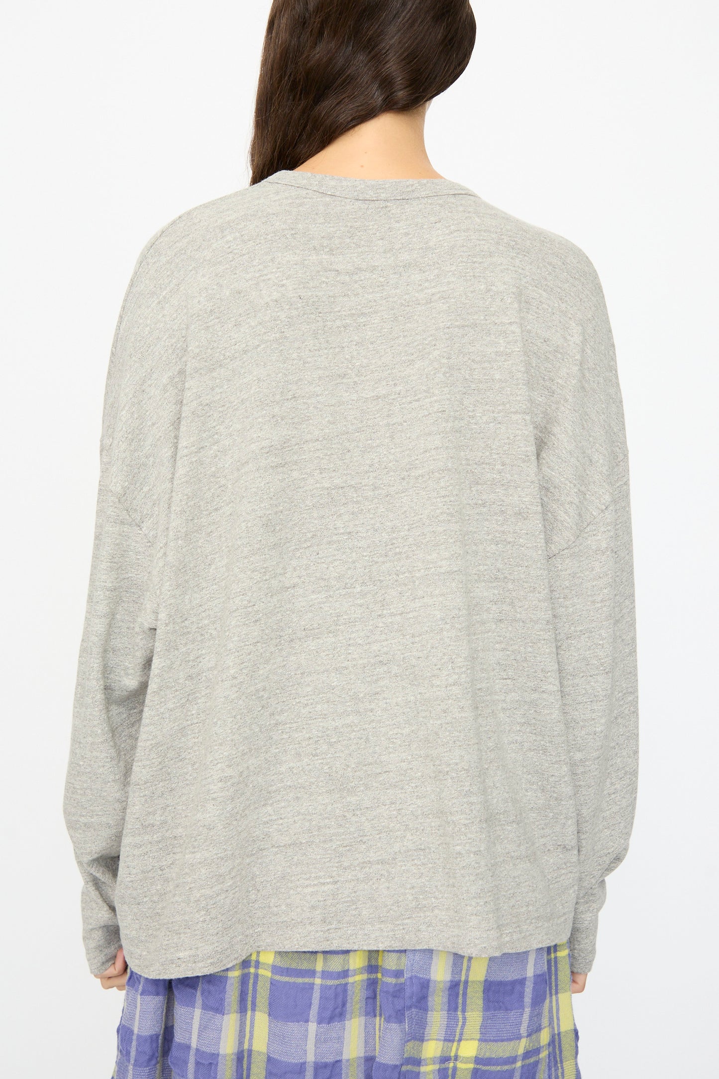 A person stands with their back to the camera, wearing the Ichi Antiquités Cotton Loose Pullover in Gray and a blue and yellow plaid skirt. This stylish Japanese-made top offers a relaxed fit.