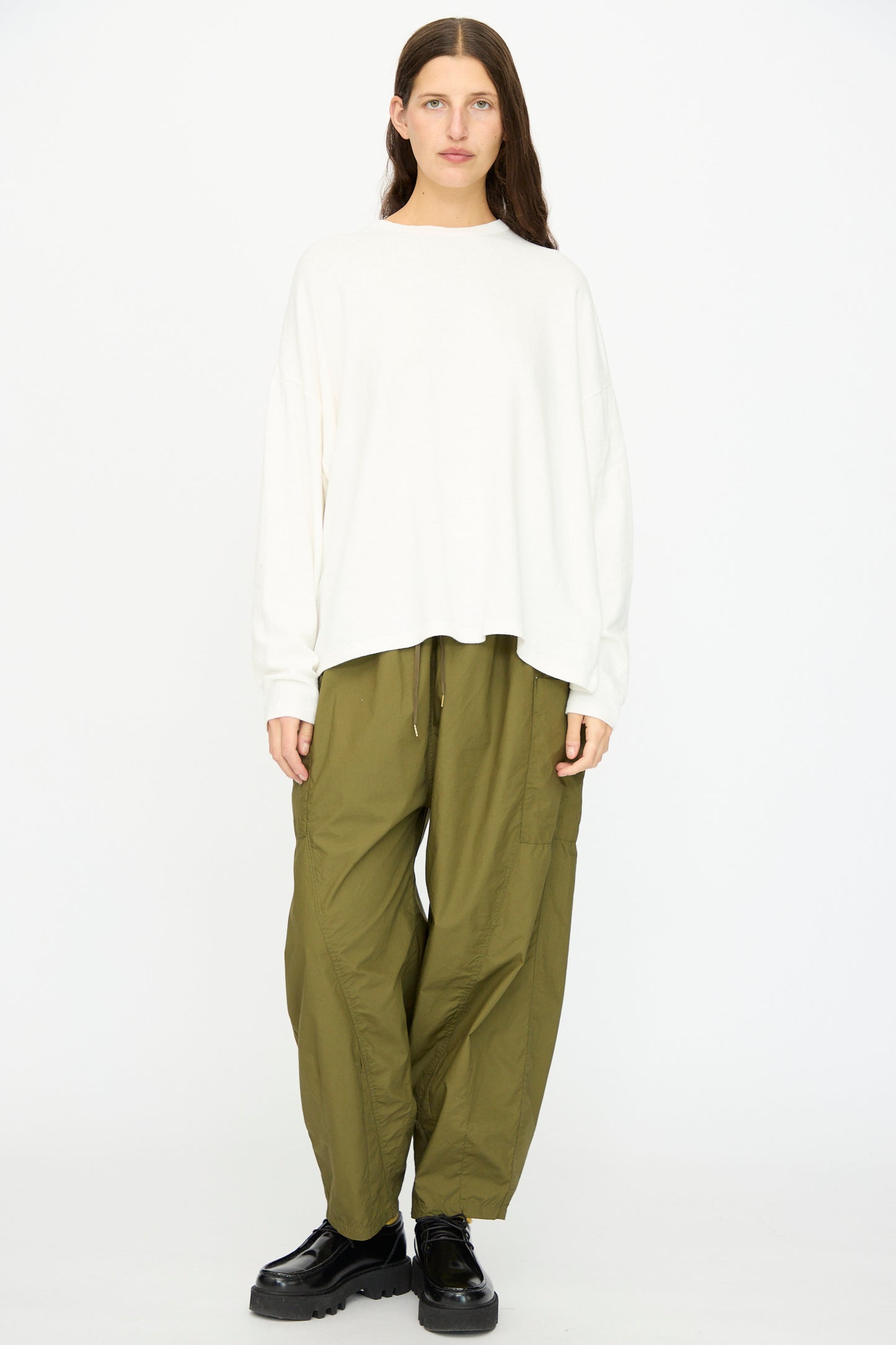 A person stands facing forward against a plain white background, wearing the Ichi Antiquités Cotton Loose Pullover in White, paired with olive green baggy pants and black platform shoes.
