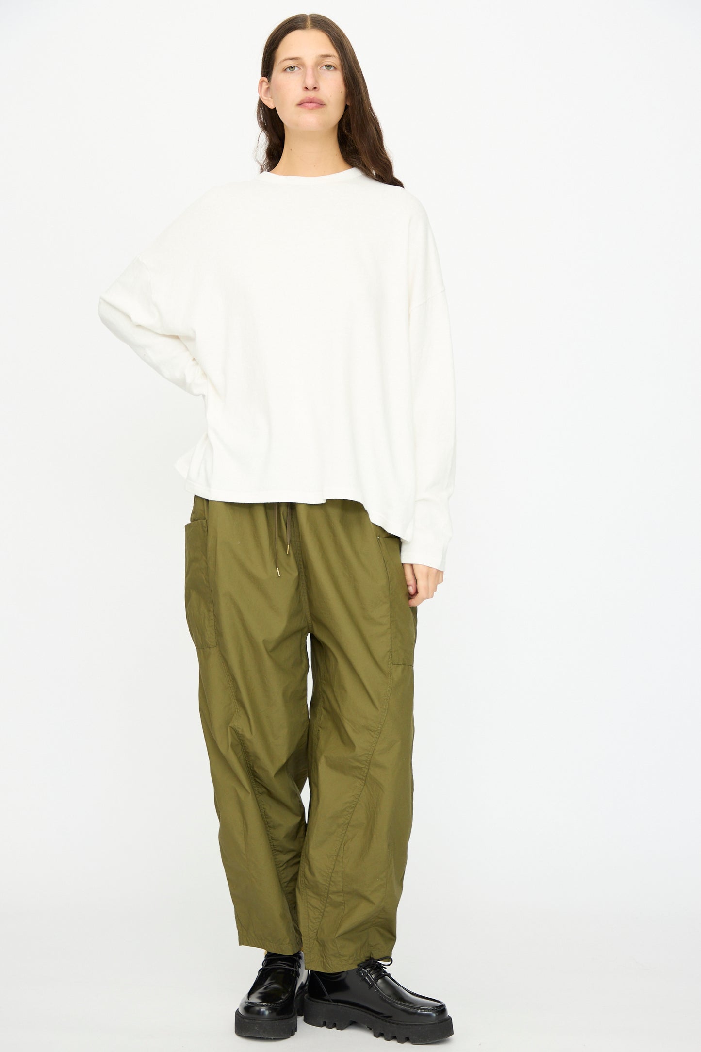 A person stands against a plain background wearing the Ichi Antiquités Cotton Loose Pullover in White, paired with loose olive green cargo pants and black platform shoes.