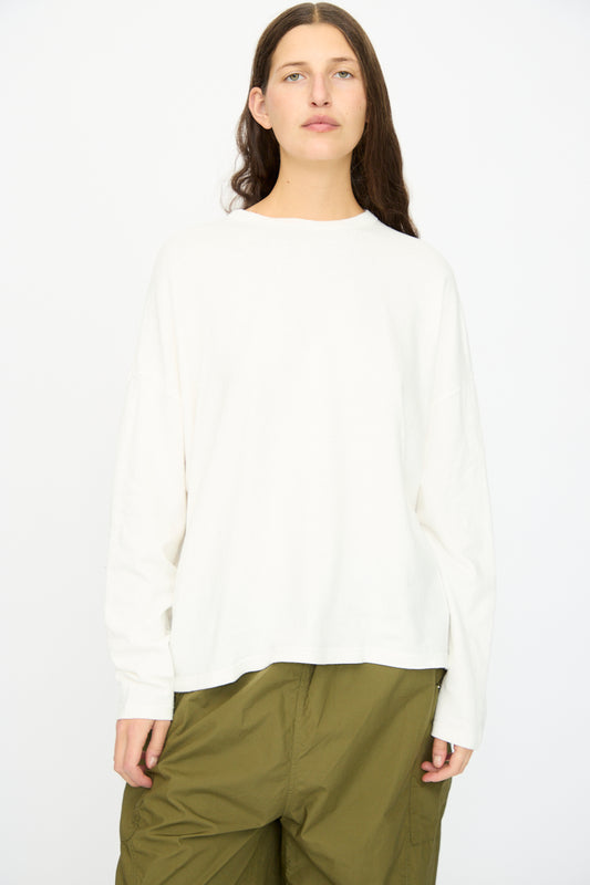 A person with long brown hair wears the Ichi Antiquités Cotton Loose Pullover in White, paired with olive green pants, standing against a plain white background.