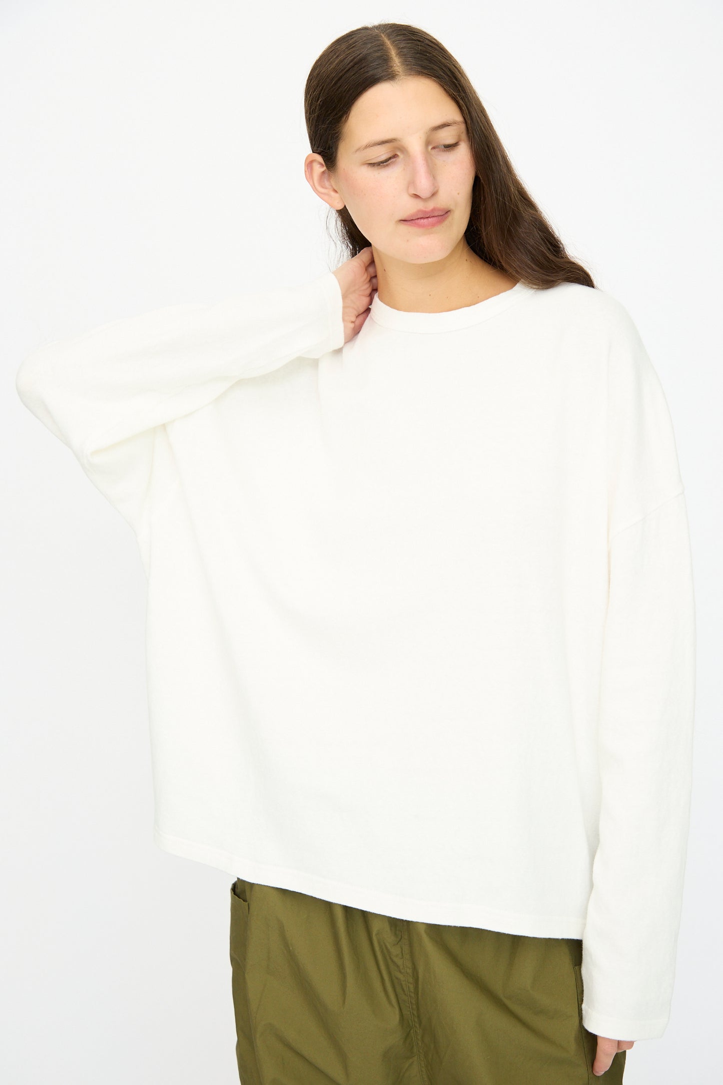 A person stands against a plain background, wearing the Ichi Antiquités Cotton Loose Pullover in White and olive green pants, with one hand touching the back of their neck.