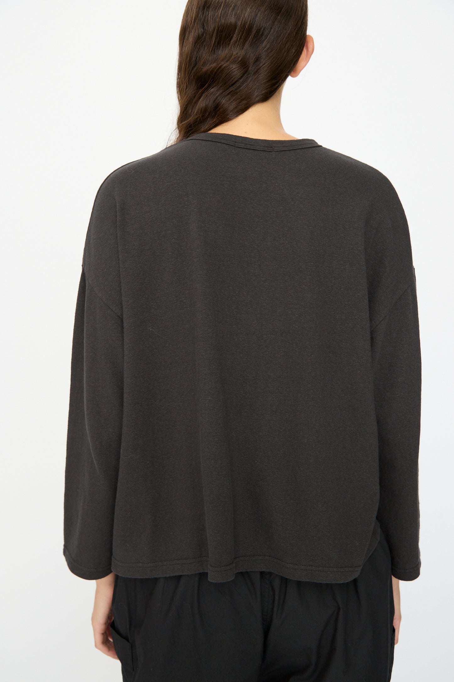 Seen from the back, a person with long brown hair wears the Ichi Antiquités Cotton Pullover in Black, styled with black pants against a simple background.