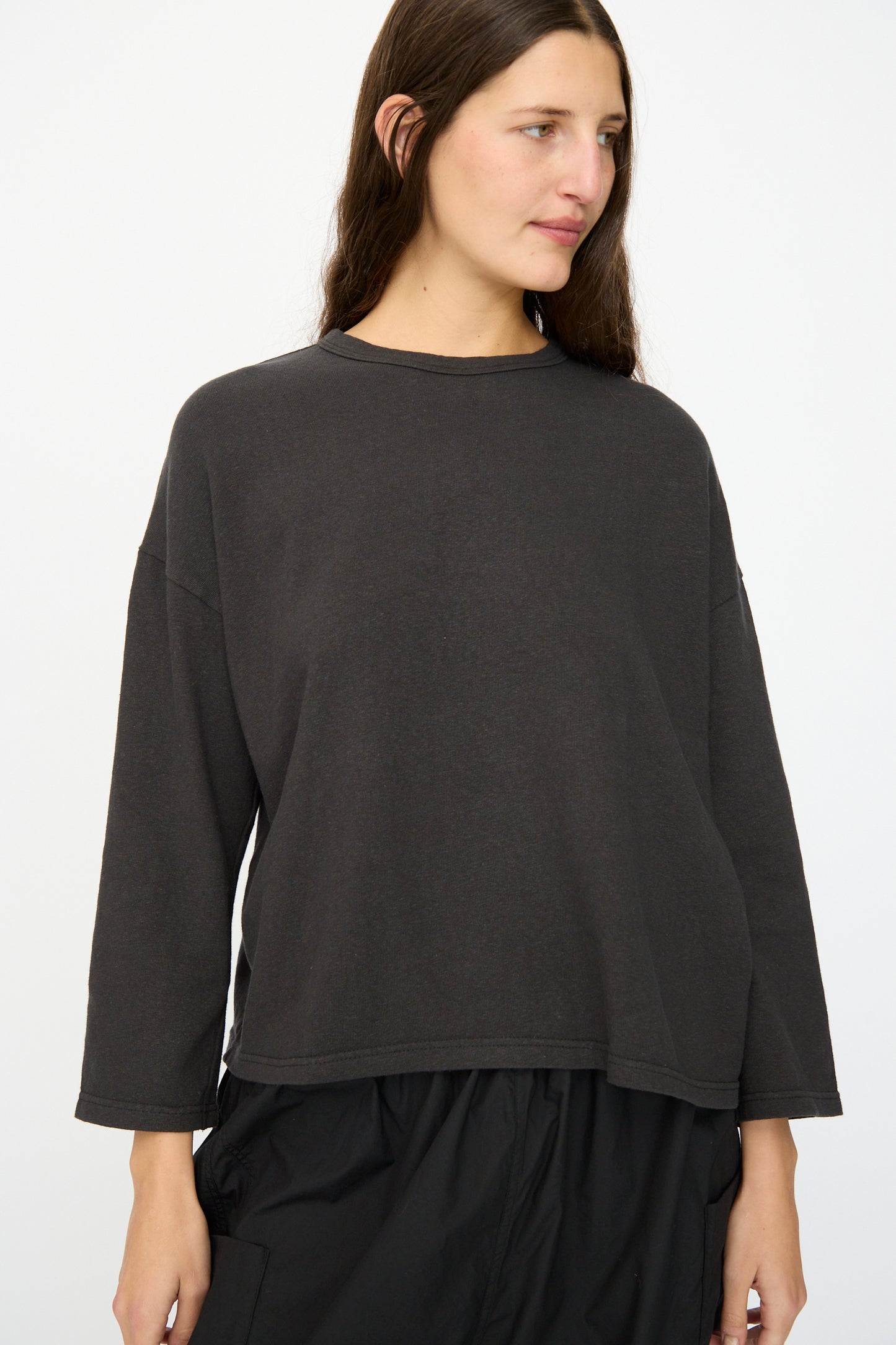 A woman with long brown hair wears the Ichi Antiquités Cotton Pullover in Black with black pants, standing against a plain white background.