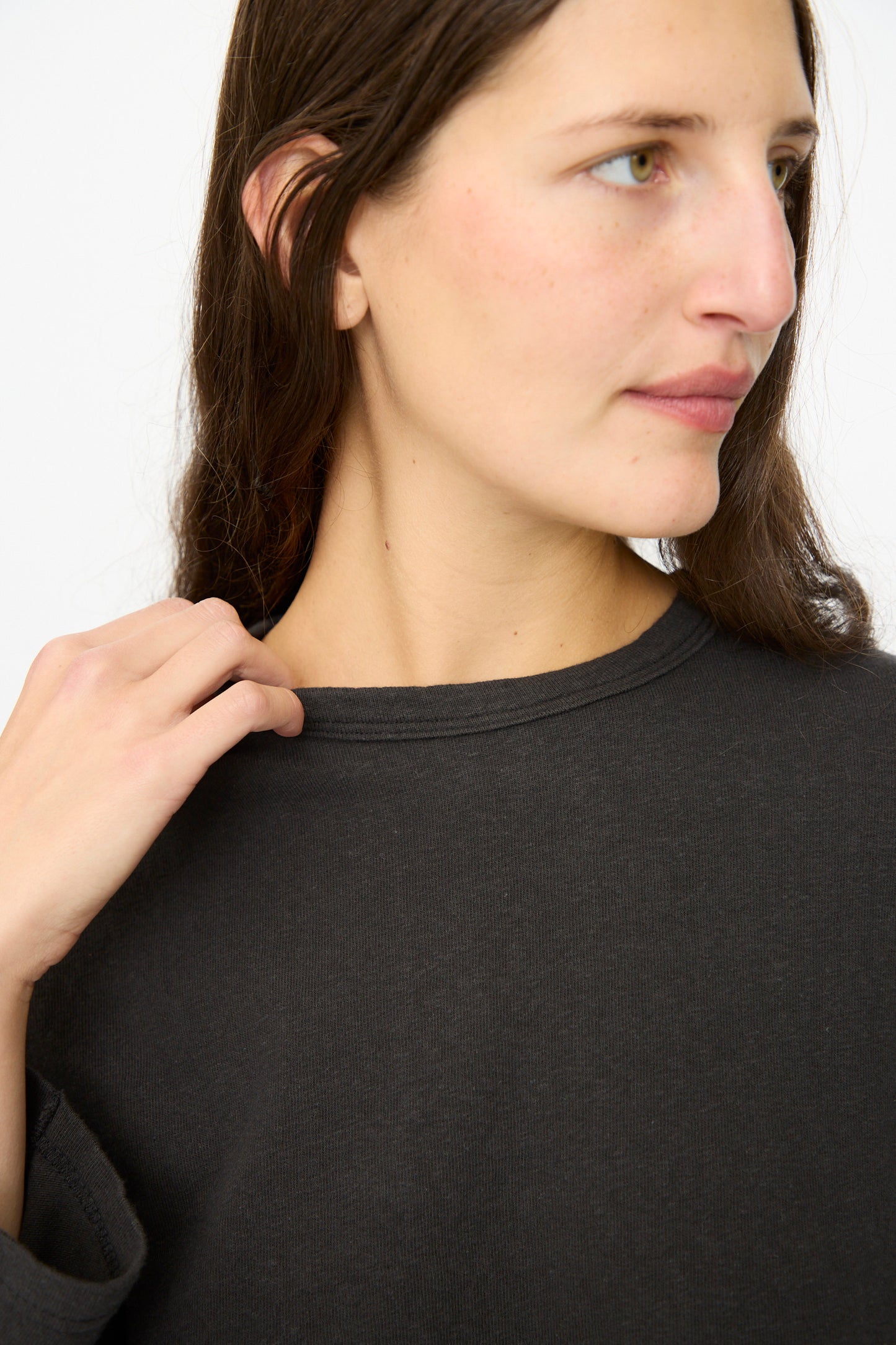 A person with long brown hair wears the Ichi Antiquités Cotton Pullover in Black, looking to the side and holding the collar against a plain light background.