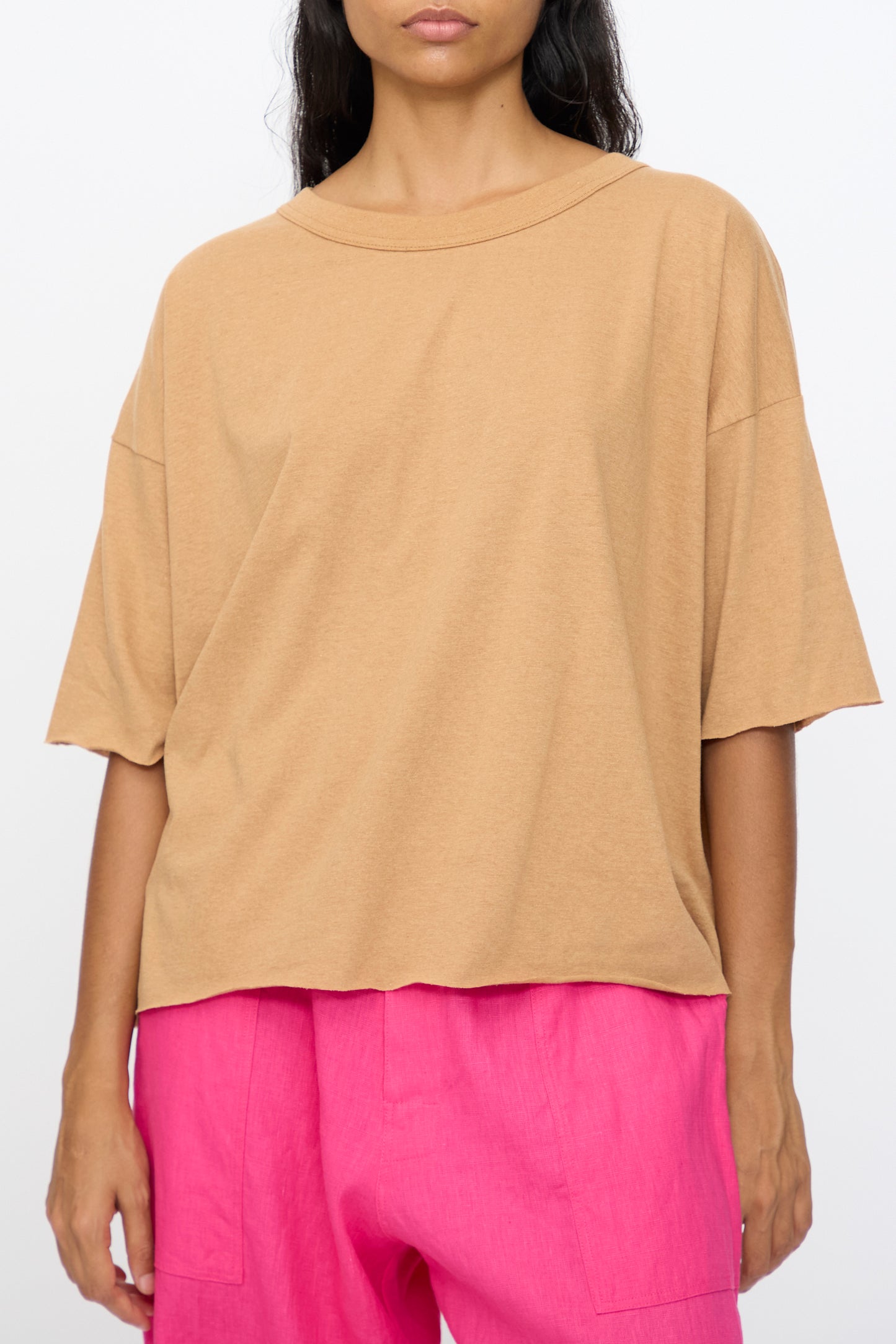 A person wears the Ichi Antiquités Cotton Pullover Tee in Camel, featuring a loose, boxy fit, paired with bright pink pants and standing against a plain white background.