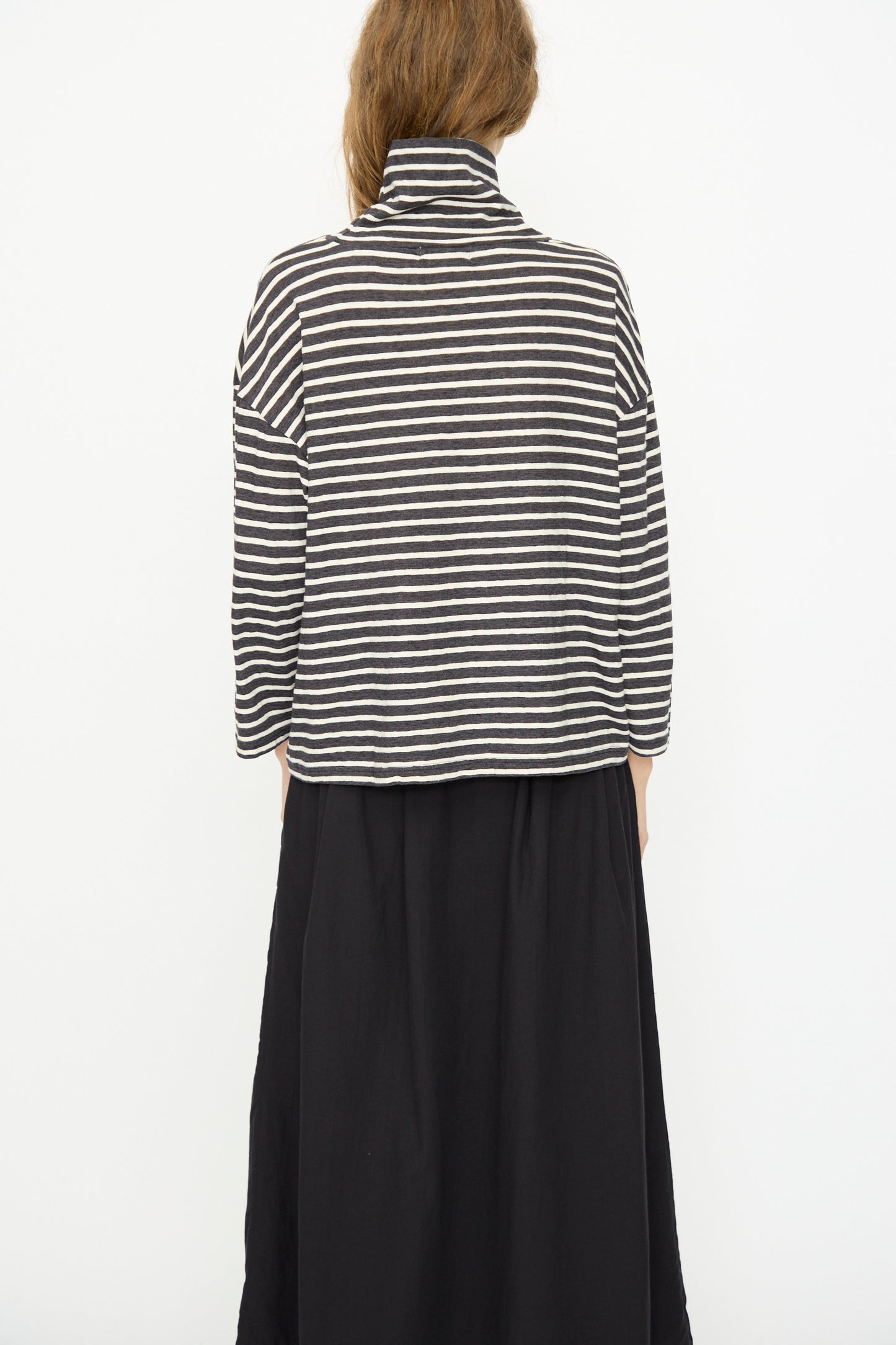 Person faces away from the camera, wearing the Ichi Antiquités Cotton Stripe Turtleneck in Charcoal with a black skirt, set against a plain white background.