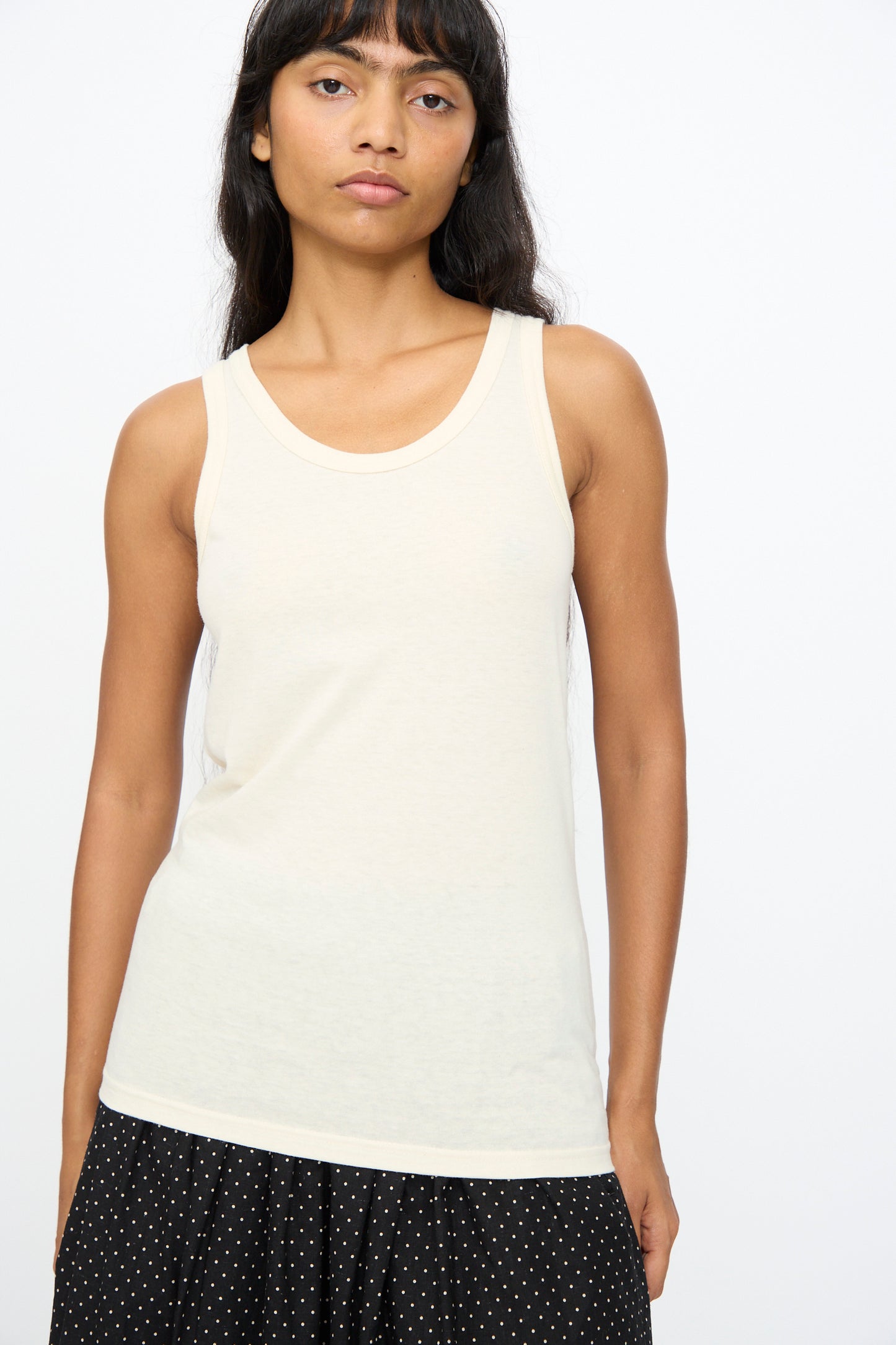 Model wearing the Ichi Antiquités Cotton Tank Top in Natural, a slim fit sleeveless off-white top, paired with a black skirt with white polka dots, standing against a plain white background.