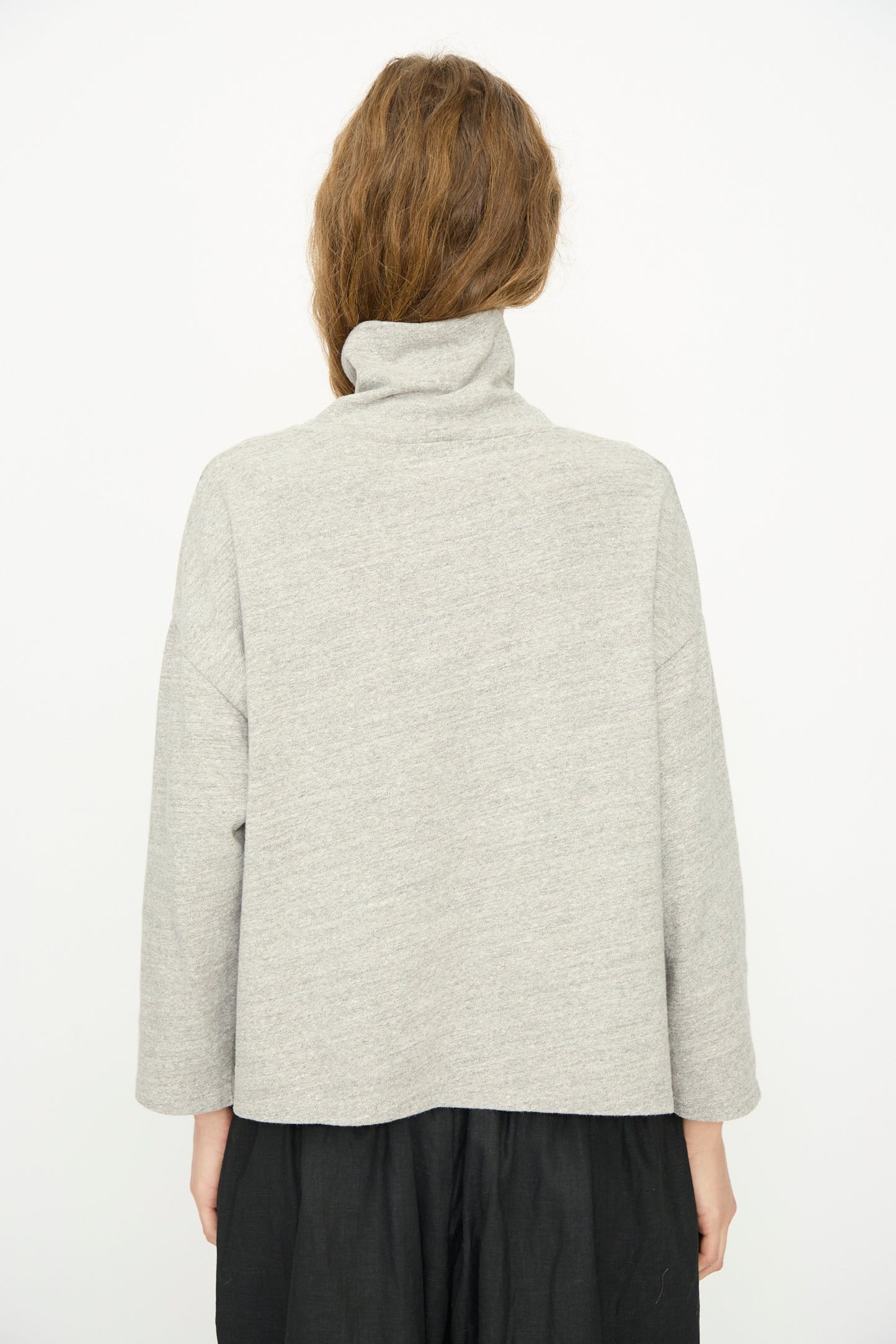 A person stands with their back to the camera, wearing the Ichi Antiquités Cotton Turtleneck in Gray paired with a black skirt, set against a plain white background.