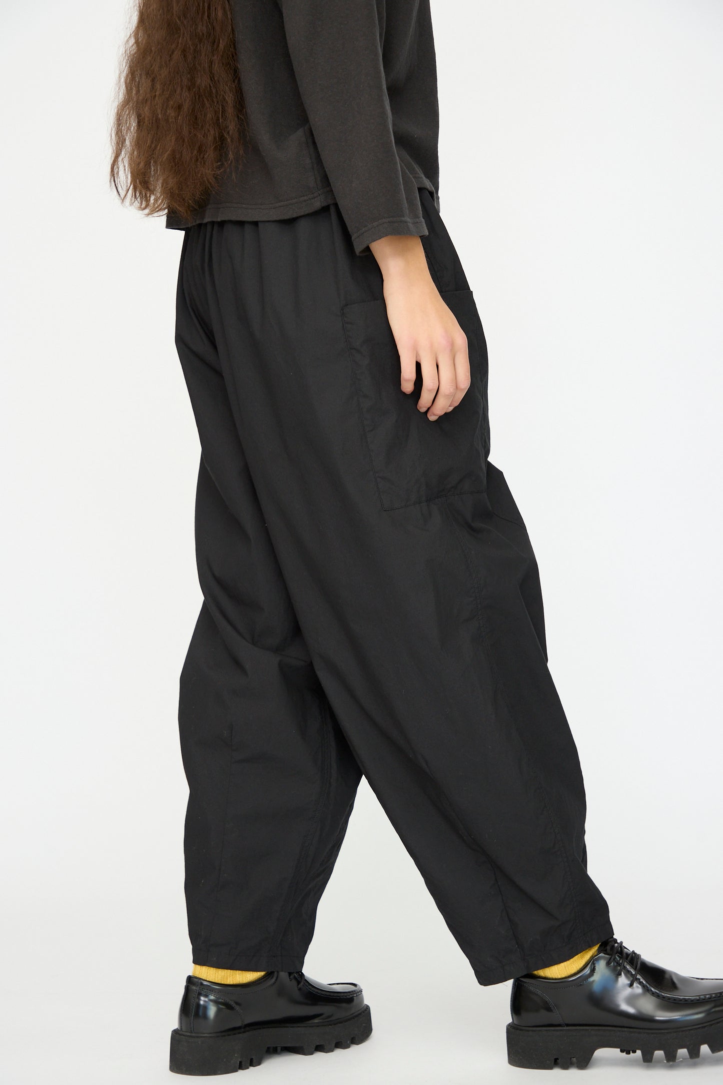 A person in Ichi Antiquités Cotton Typewriter Pants in Black, a dark long-sleeve top, yellow socks, and black shoes stands against a plain light background.