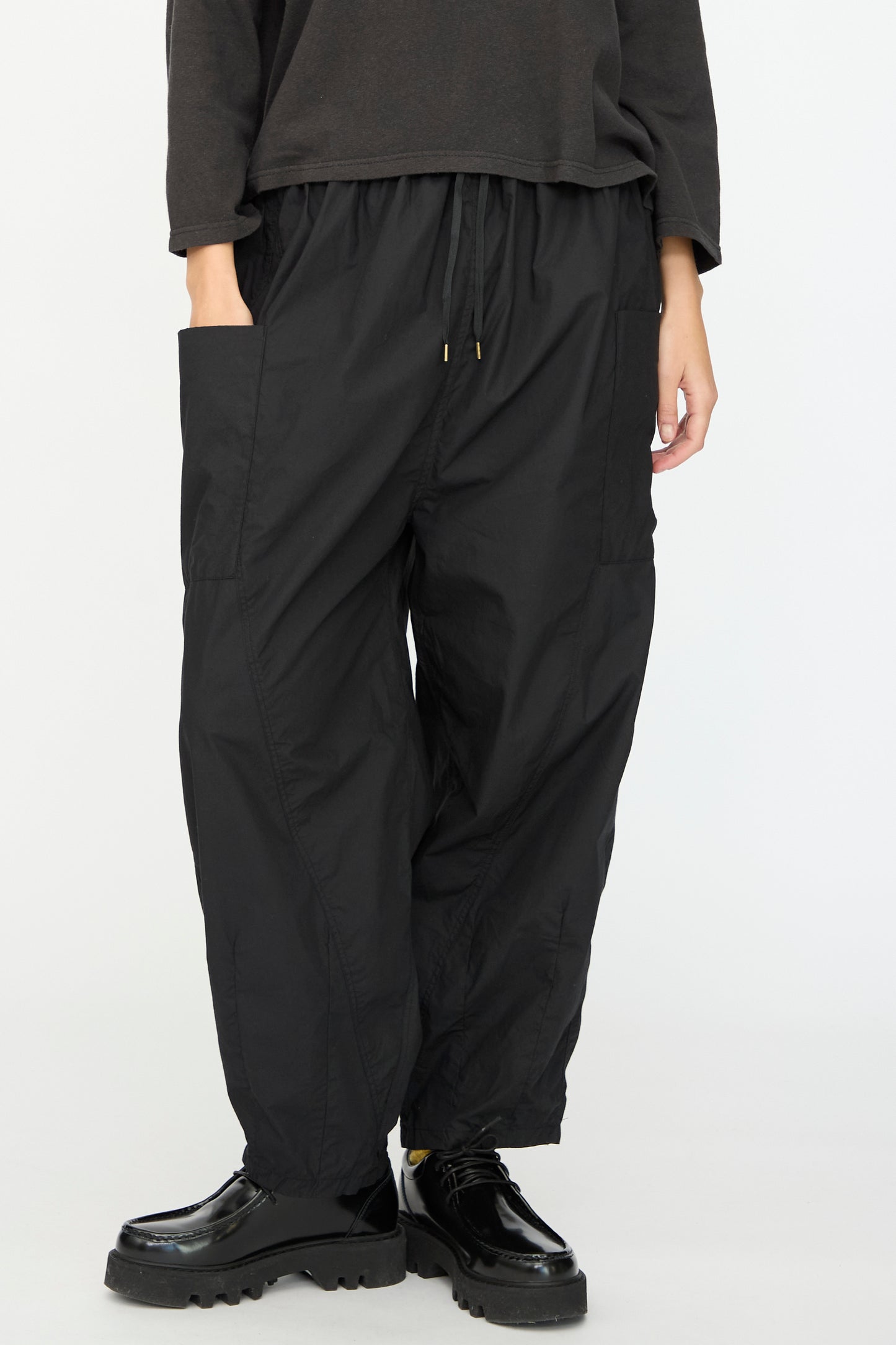 A person wears Ichi Antiquités’ Cotton Typewriter Pants in Black—loose fit with a drawstring waist and large side pockets—paired with black platform shoes, standing against a plain light background. Made in Japan.