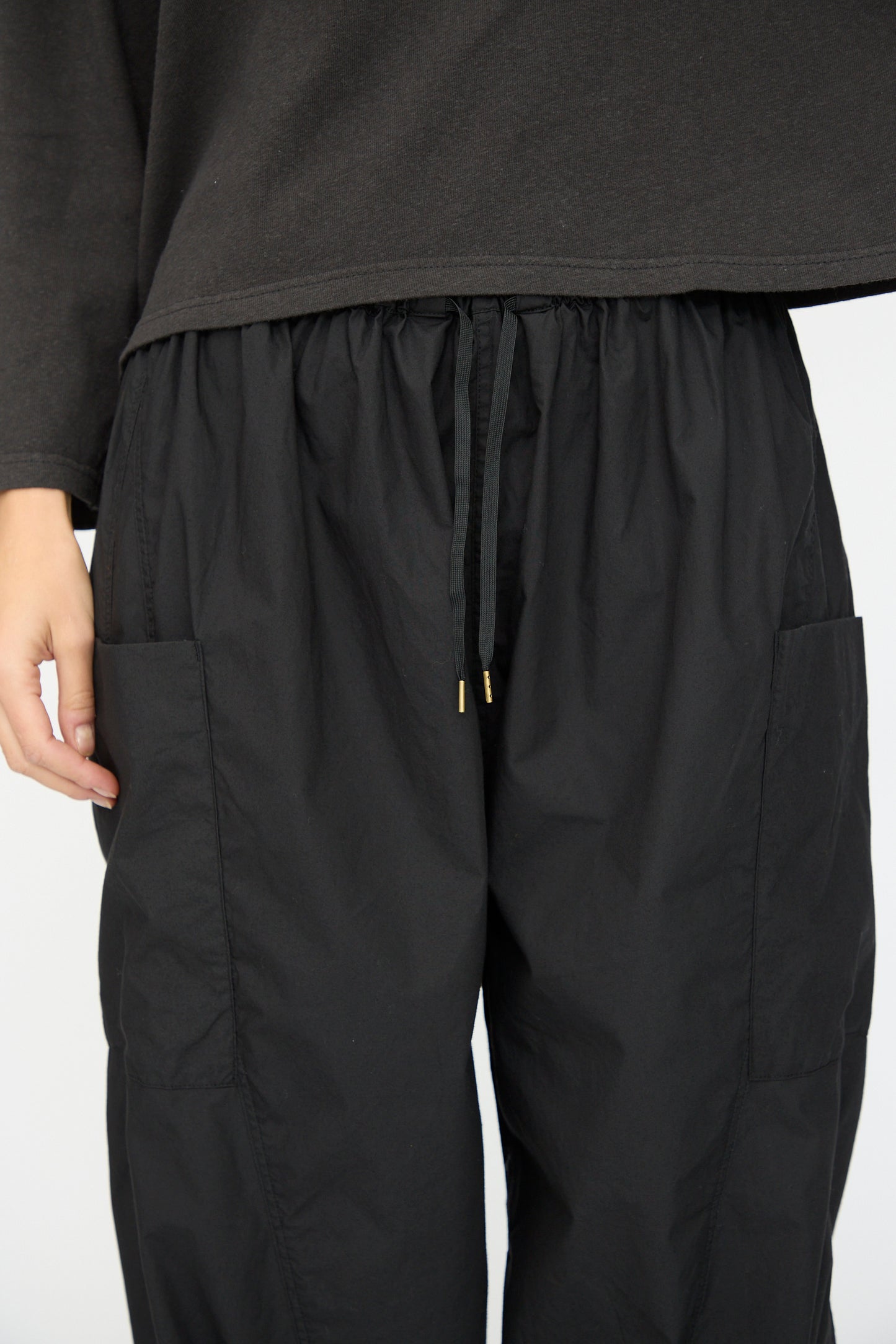 A person wearing Ichi Antiquités' Cotton Typewriter Pants in Black with a loose black long-sleeve shirt, shown from mid-torso to knees.