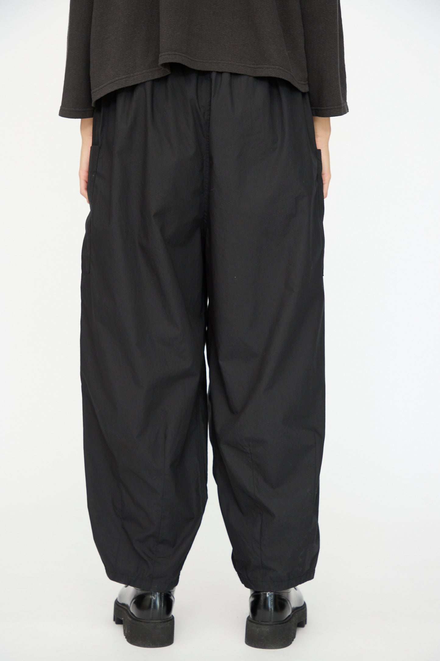 A person wearing Ichi Antiquités Cotton Typewriter Pants in Black, paired with a black top and shoes, stands against a plain white background, shown from the back.