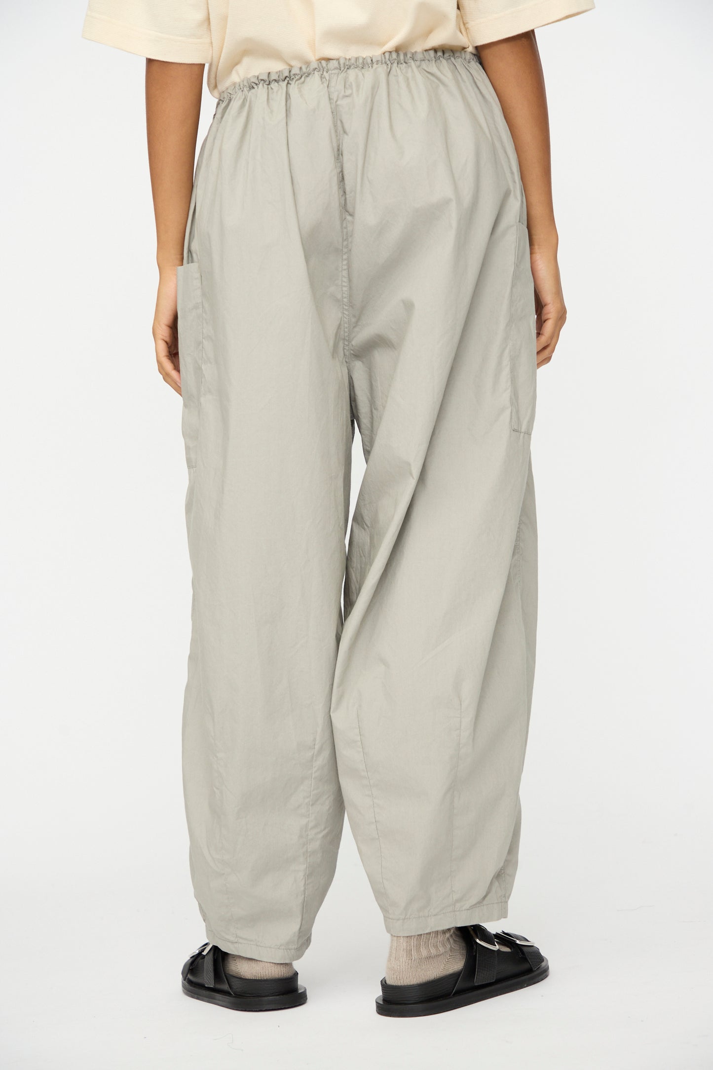 A person wearing Ichi Antiquités Cotton Typewriter Pants in gray, a beige shirt, gray socks, and black sandals stands against a plain white background.