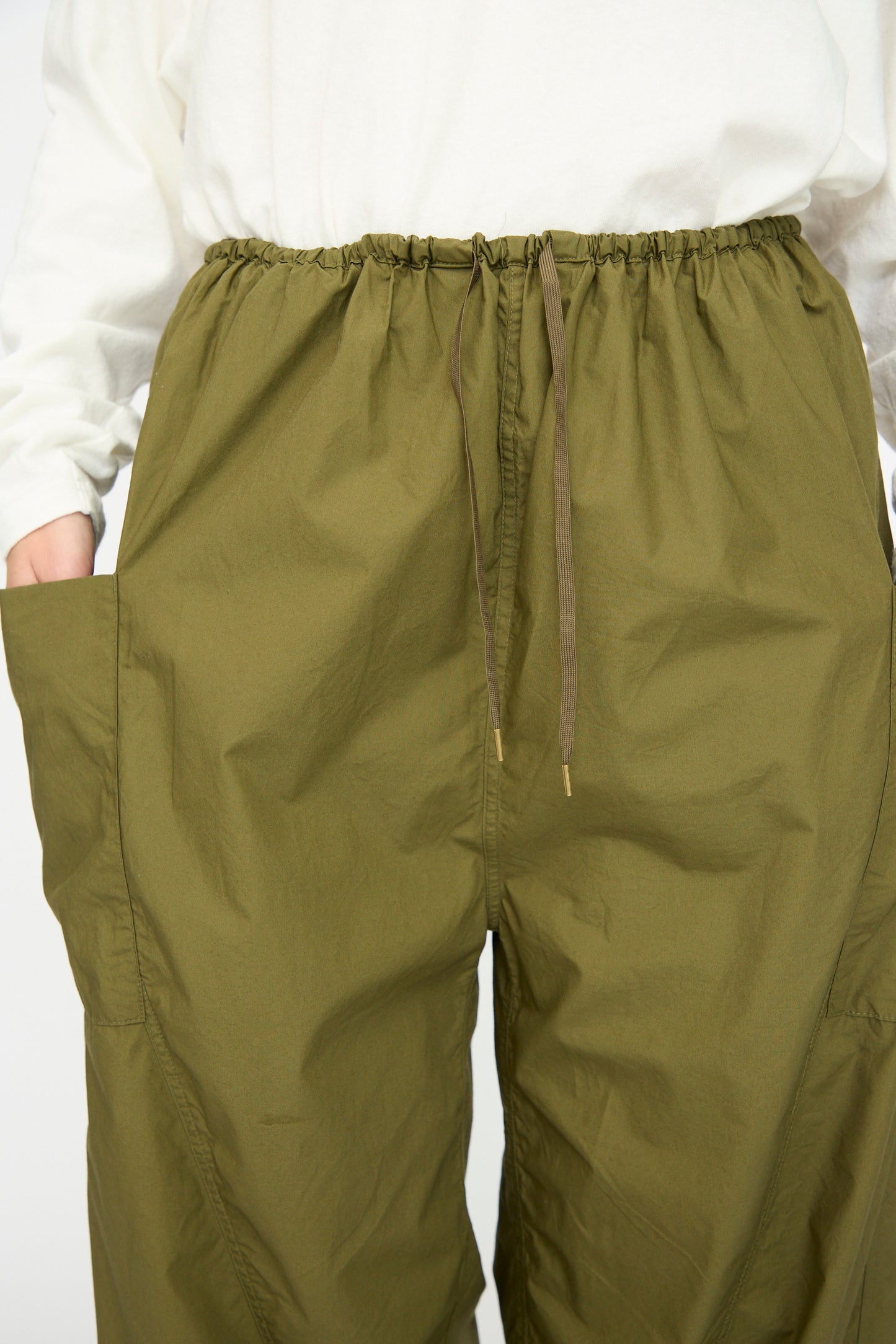 A person wears Ichi Antiquités Cotton Typewriter Pants in khaki—loose, with large side pockets—paired with a white long-sleeve shirt. Made in Japan, these pants blend comfort, utility, and style.