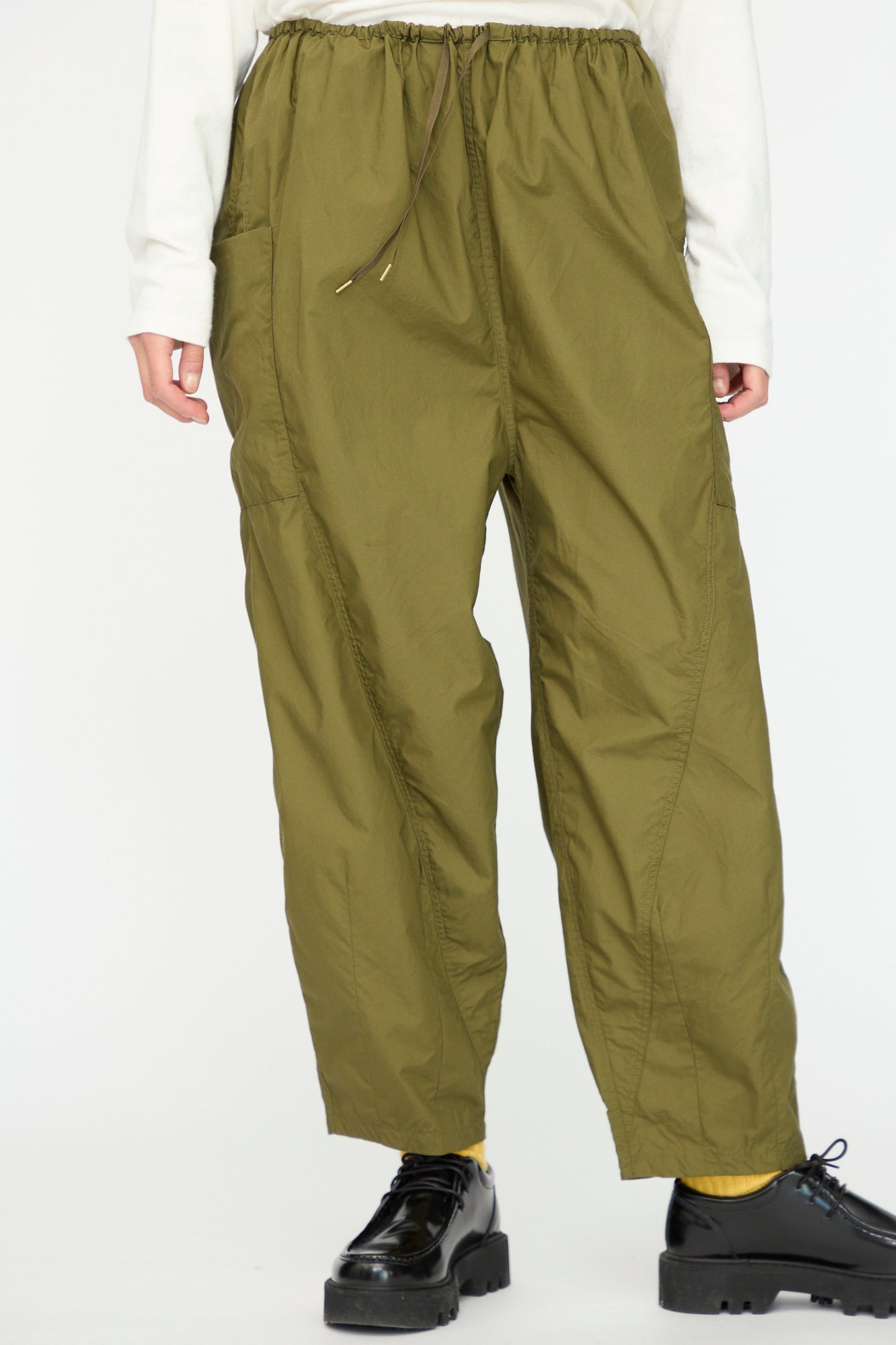 A person wearing Ichi Antiquités Cotton Typewriter Pants in khaki, paired with a white long-sleeve shirt, yellow socks, and black platform shoes, stands against a plain background.