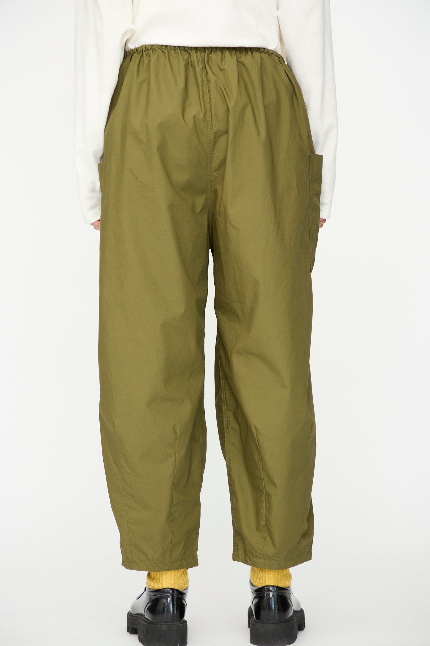 Person wearing Ichi Antiquités Cotton Typewriter Pants in khaki, yellow socks, black shoes, and a white long-sleeve top, photographed from the back against a plain background.
