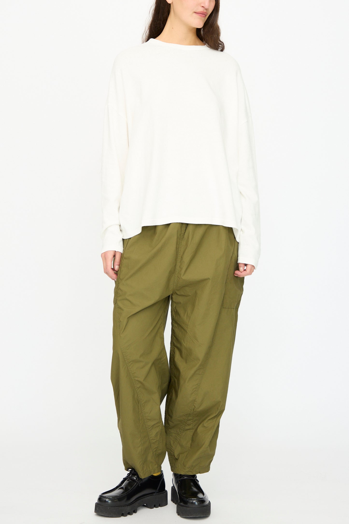 A person wearing loose Cotton Typewriter Pants in Khaki by Ichi Antiquités, a loose white long-sleeve shirt, and black platform shoes stands against a plain white background.