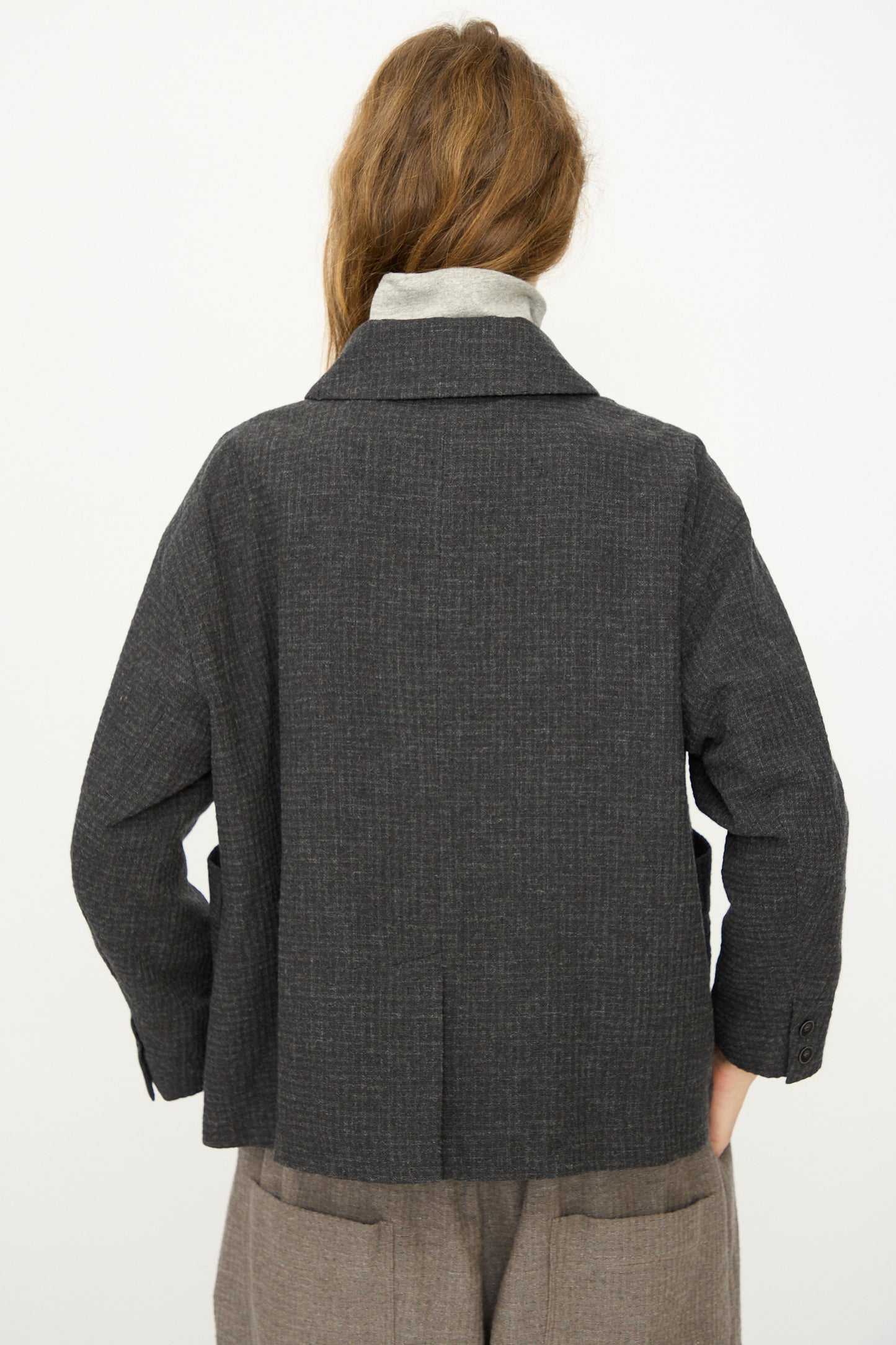 A person stands with their back to the camera, wearing the Ichi Antiquités Cotton Wool Sucker Jacket in Charcoal over a light gray turtleneck and brown pants.
