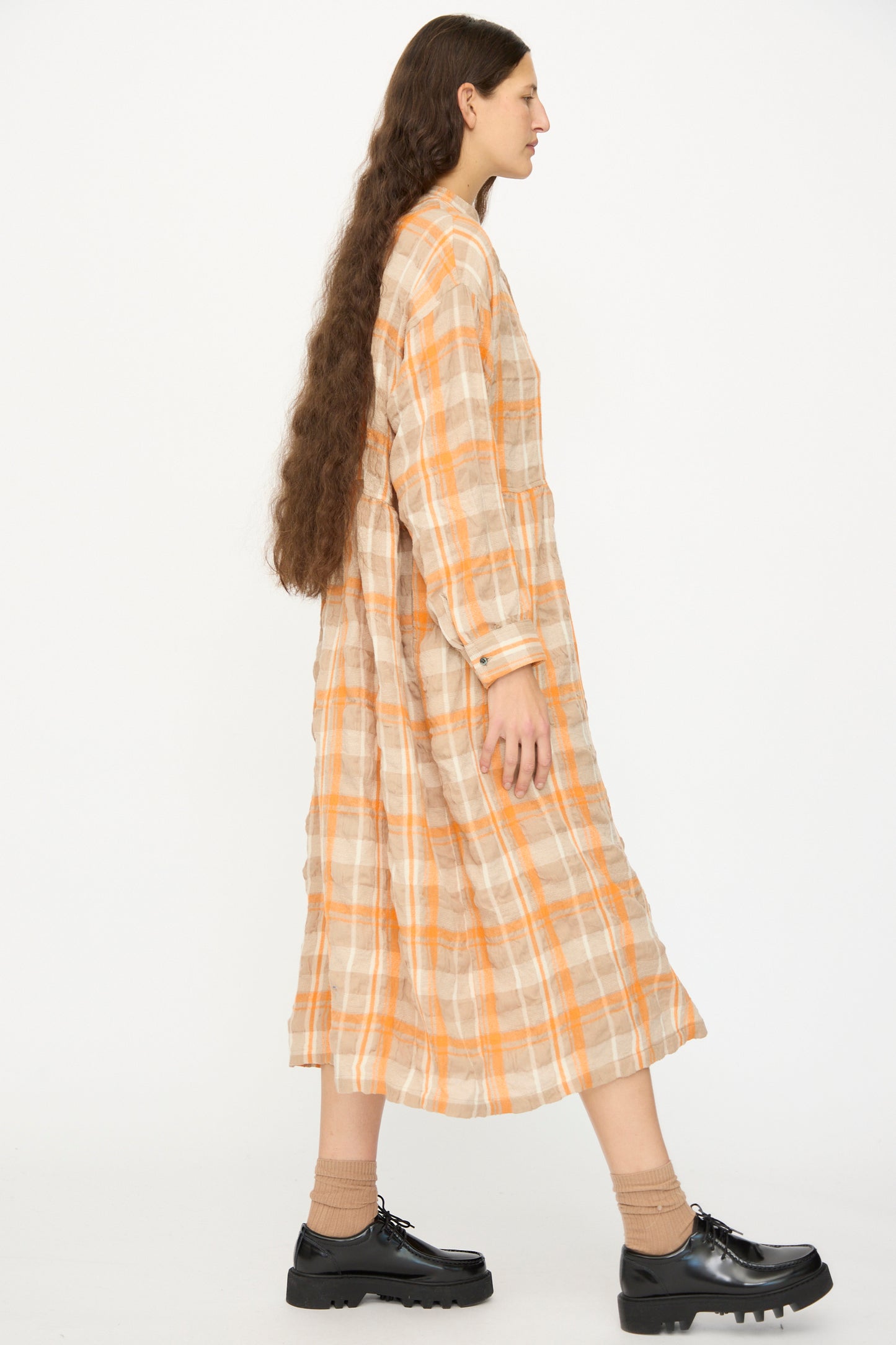 A person with long brown hair stands in profile against a plain white background, wearing the Ichi Antiquités Cotton Wool Tartan Check Dress in Orange.