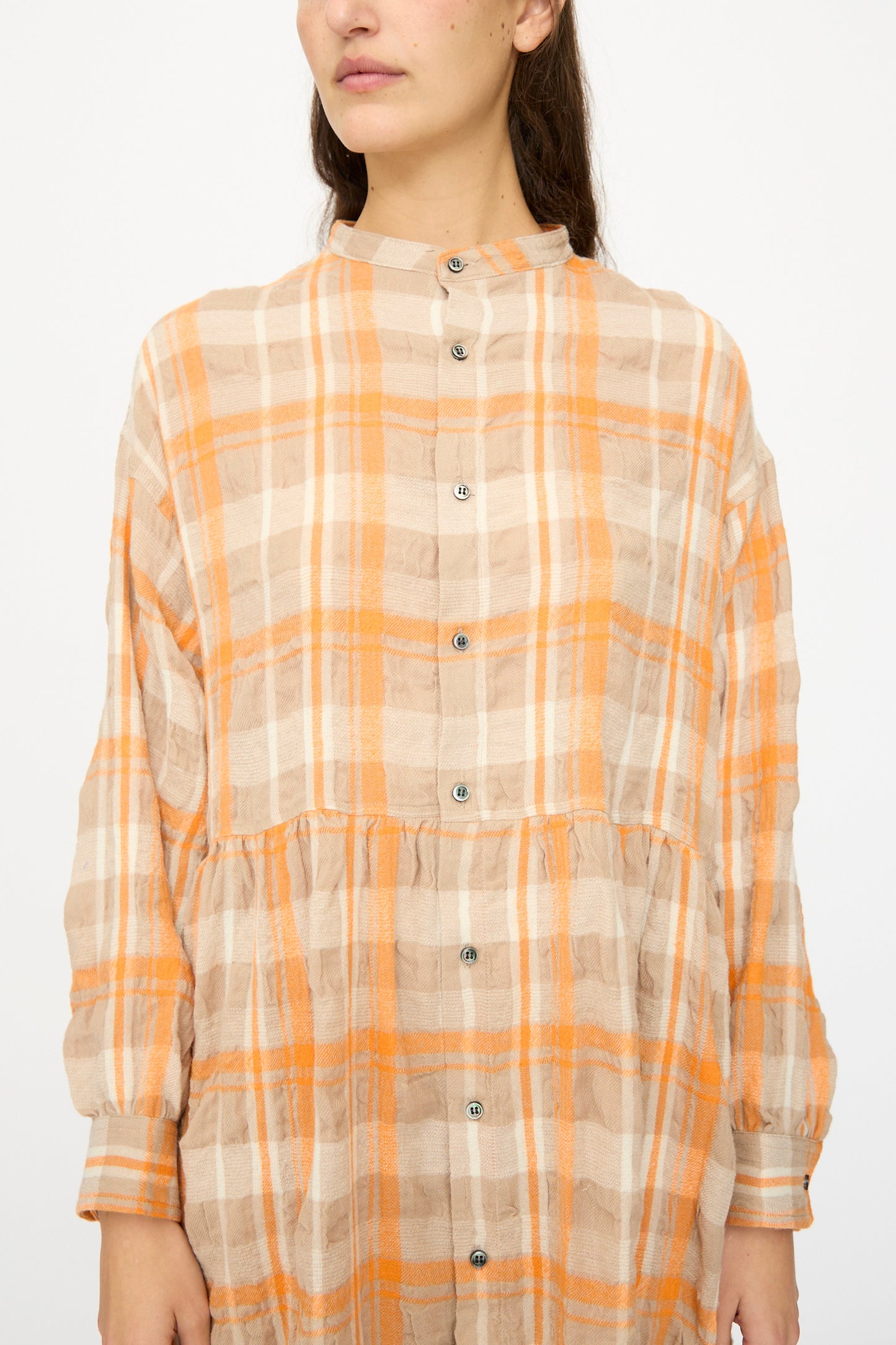 A person wears the Ichi Antiquités Cotton Wool Tartan Check Dress in Orange, featuring long sleeves, an oversized silhouette, and a button-down front with an orange and beige plaid pattern, standing against a plain white background.