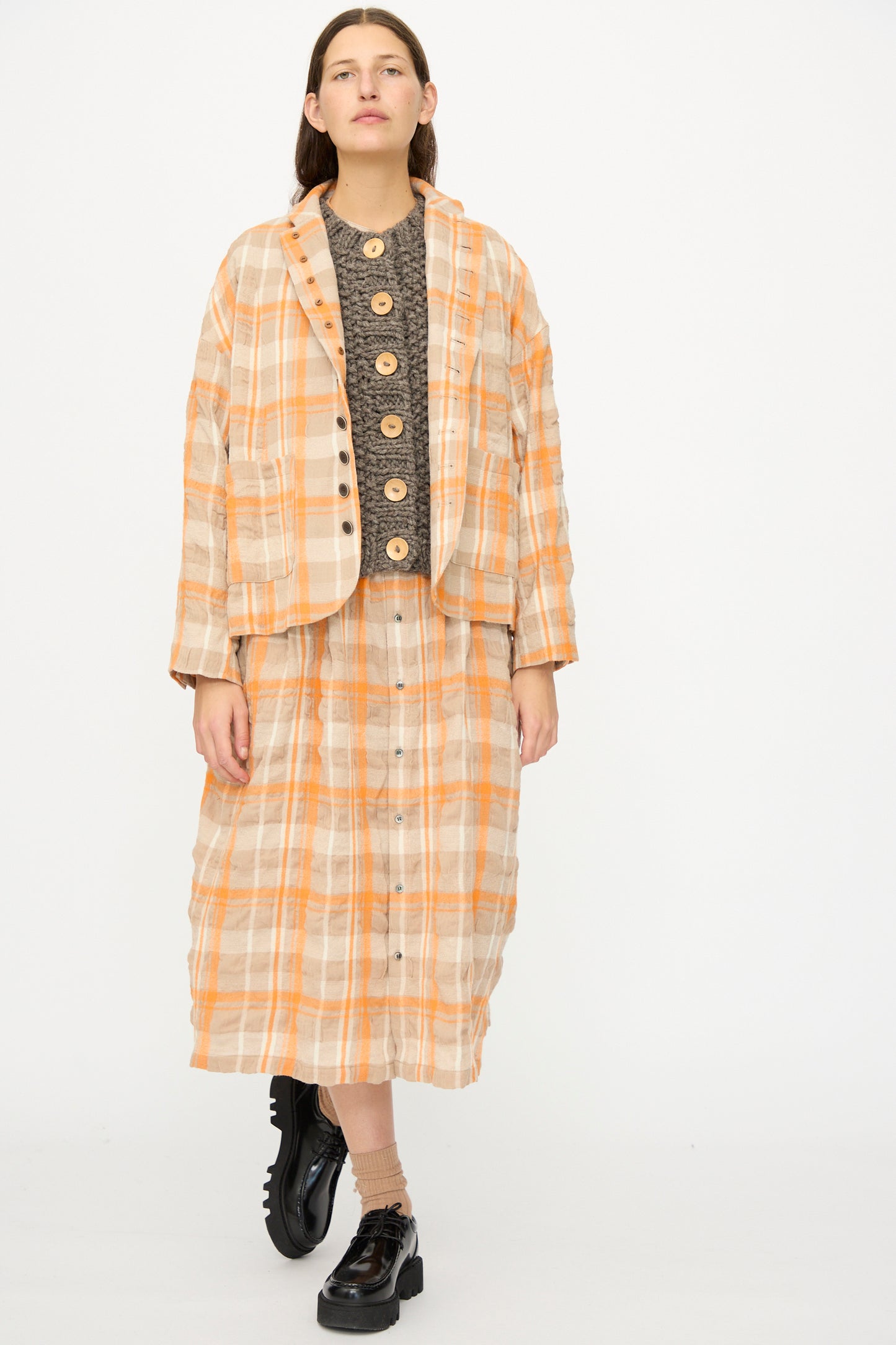 A person wears the Ichi Antiquités Cotton Wool Tartan Check Jacket in Orange, styled with a dark textured top, matching skirt, and black chunky shoes, standing against a plain white background.