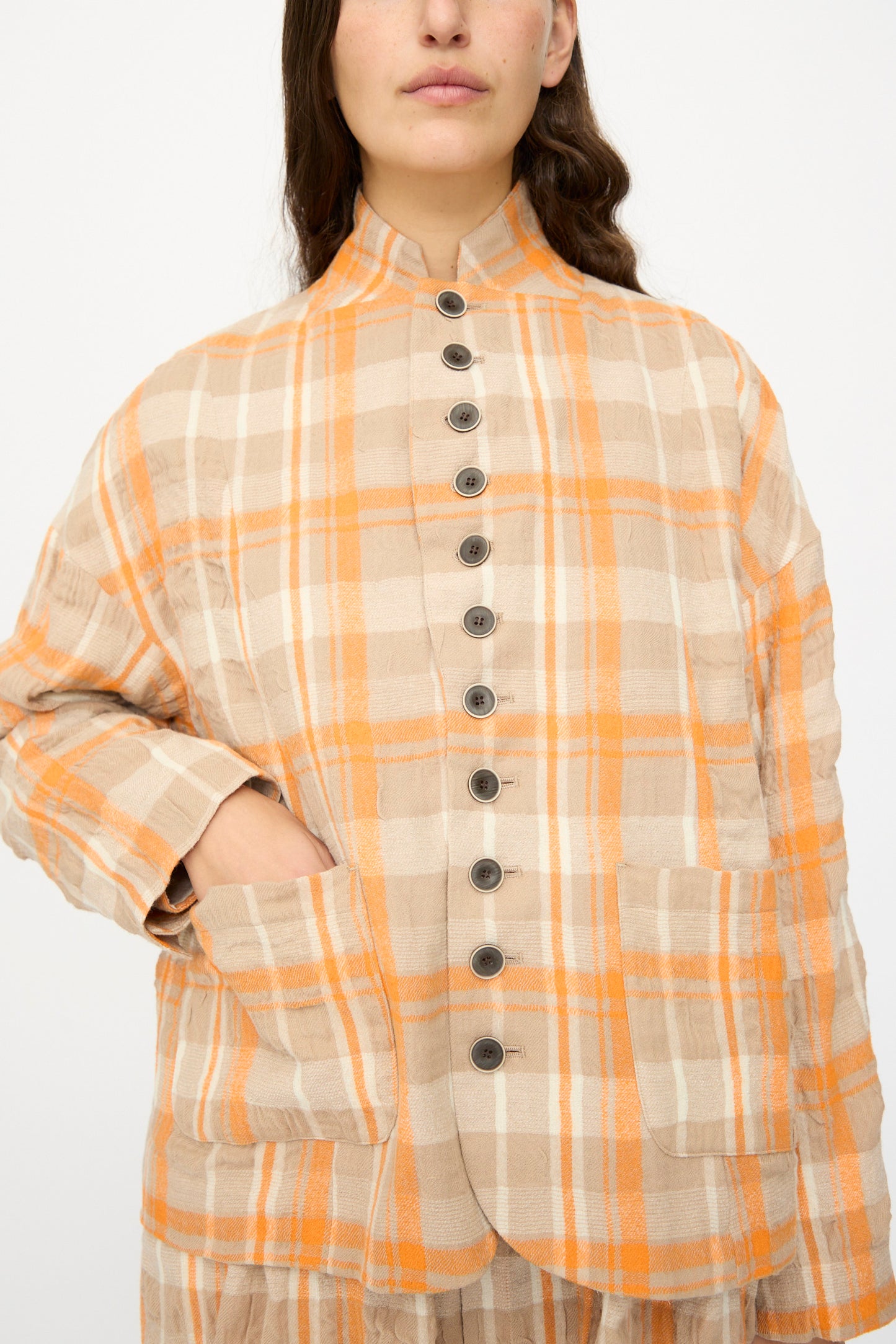 A person wearing the Ichi Antiquités Cotton Wool Tartan Check Jacket in orange, featuring beige, orange, and white checks with front pockets, stands against a plain background.
