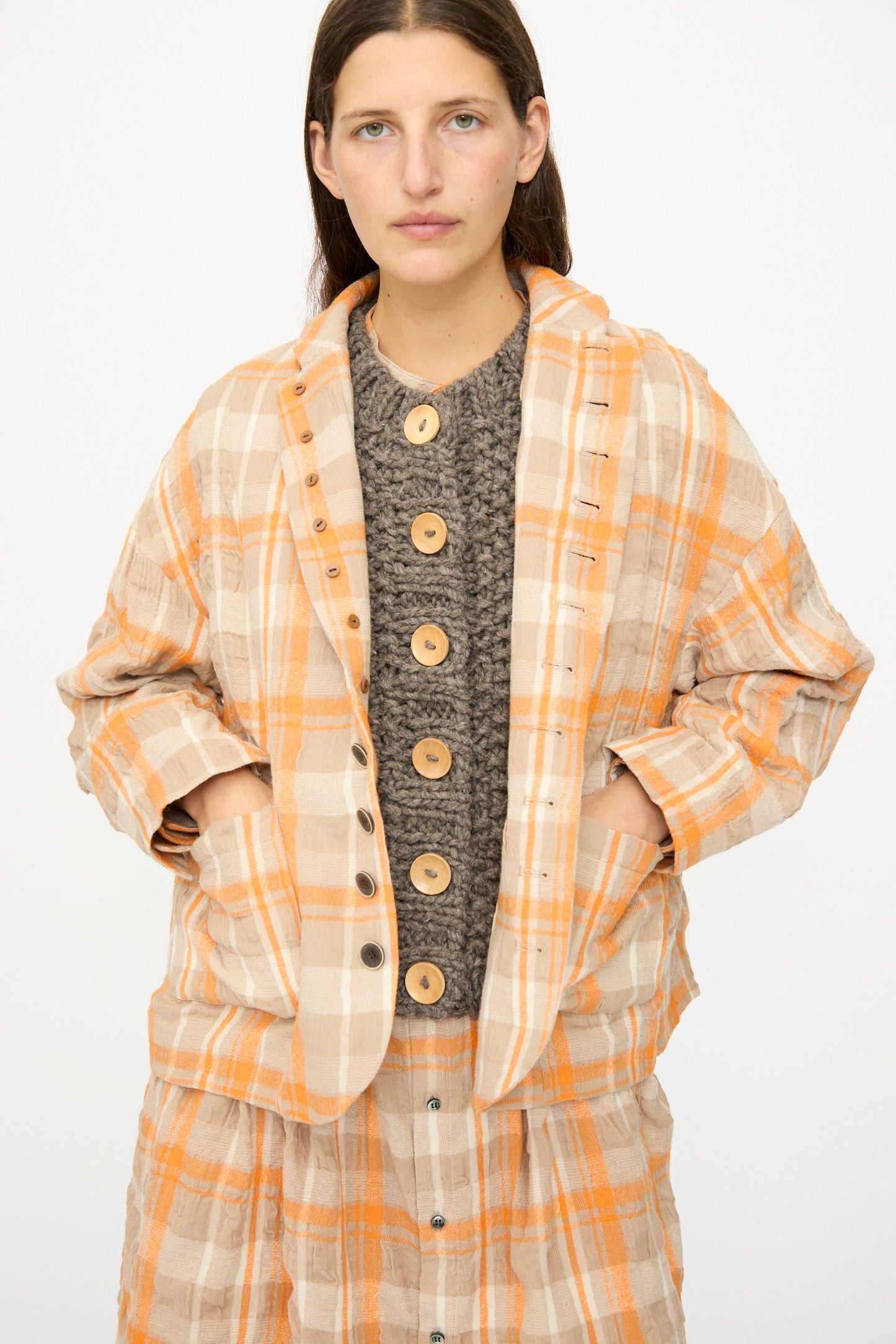 A person wears the Ichi Antiquités Cotton Wool Tartan Check Jacket in Orange over a chunky knit sweater with large wooden buttons, standing against a plain white background.
