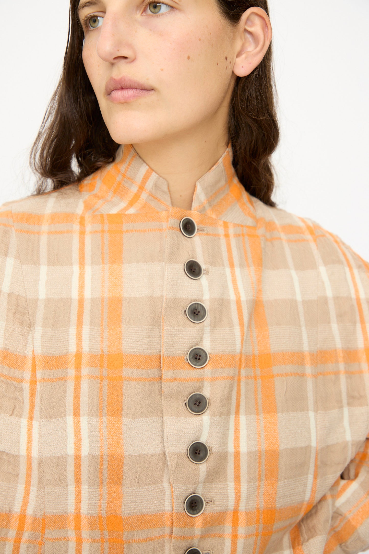 A person wearing the Ichi Antiquités Cotton Wool Tartan Check Jacket in Orange, a lightweight beige, orange, and white plaid layer with a stand collar and dark front buttons.