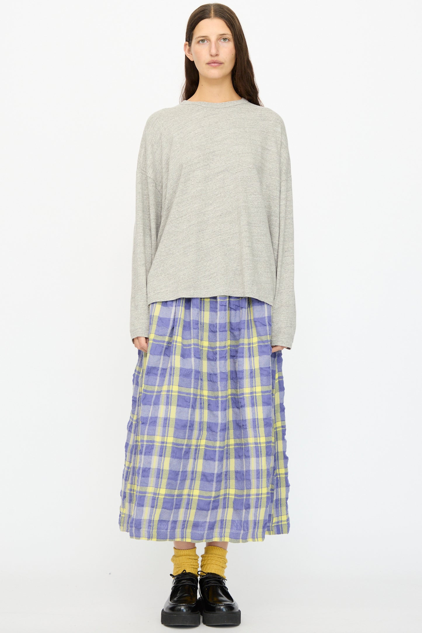 A woman faces forward wearing a loose gray long-sleeve shirt, the Ichi Antiquités Cotton Wool Tartan Check Skirt in Blue with an elastic waist, yellow socks, and black shoes against a plain white background.