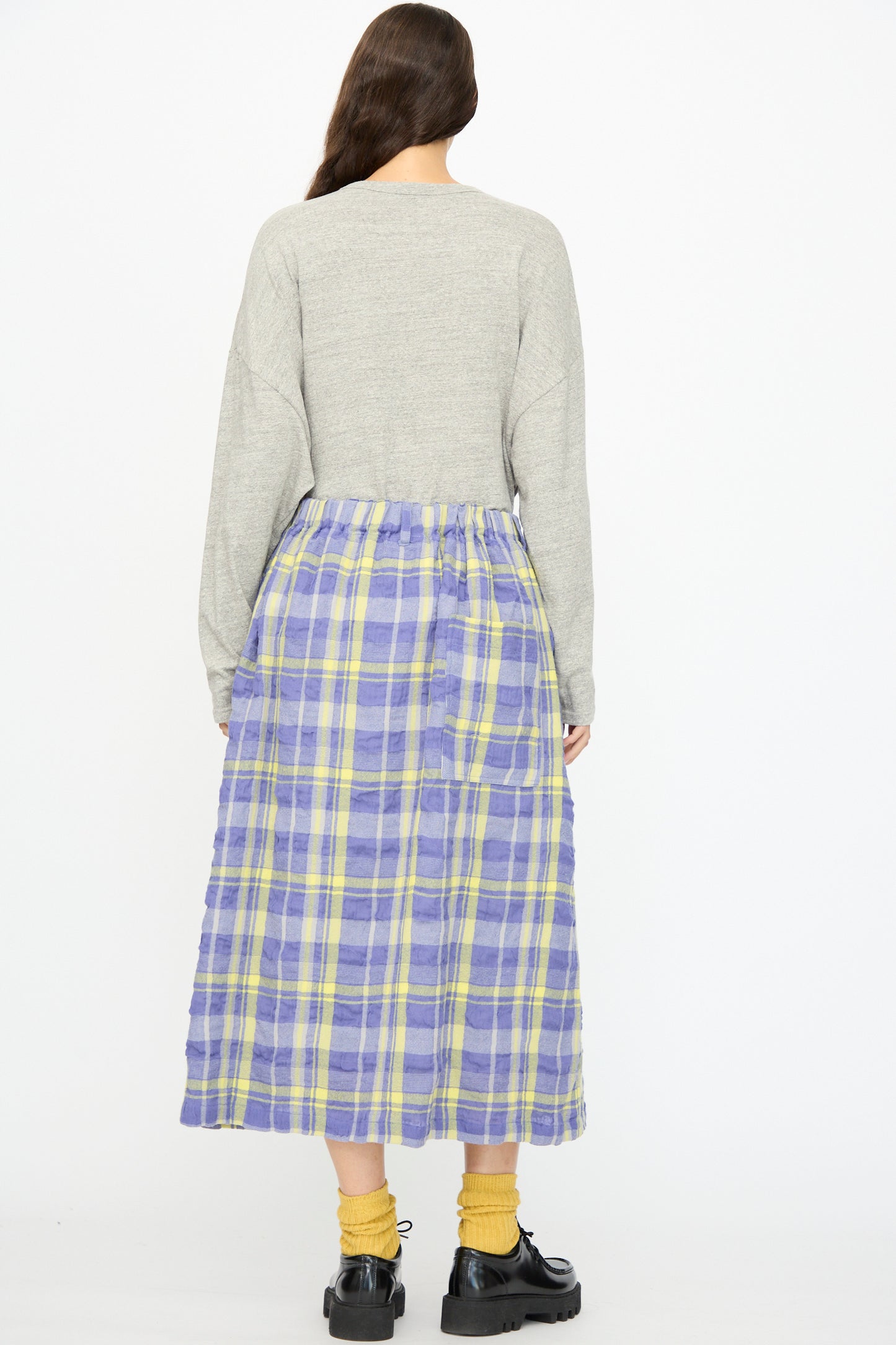 A person stands with their back to the camera, wearing a grey long-sleeve top, yellow socks, black shoes, and the Ichi Antiquités Cotton Wool Tartan Check Skirt in Blue with an elastic waist.