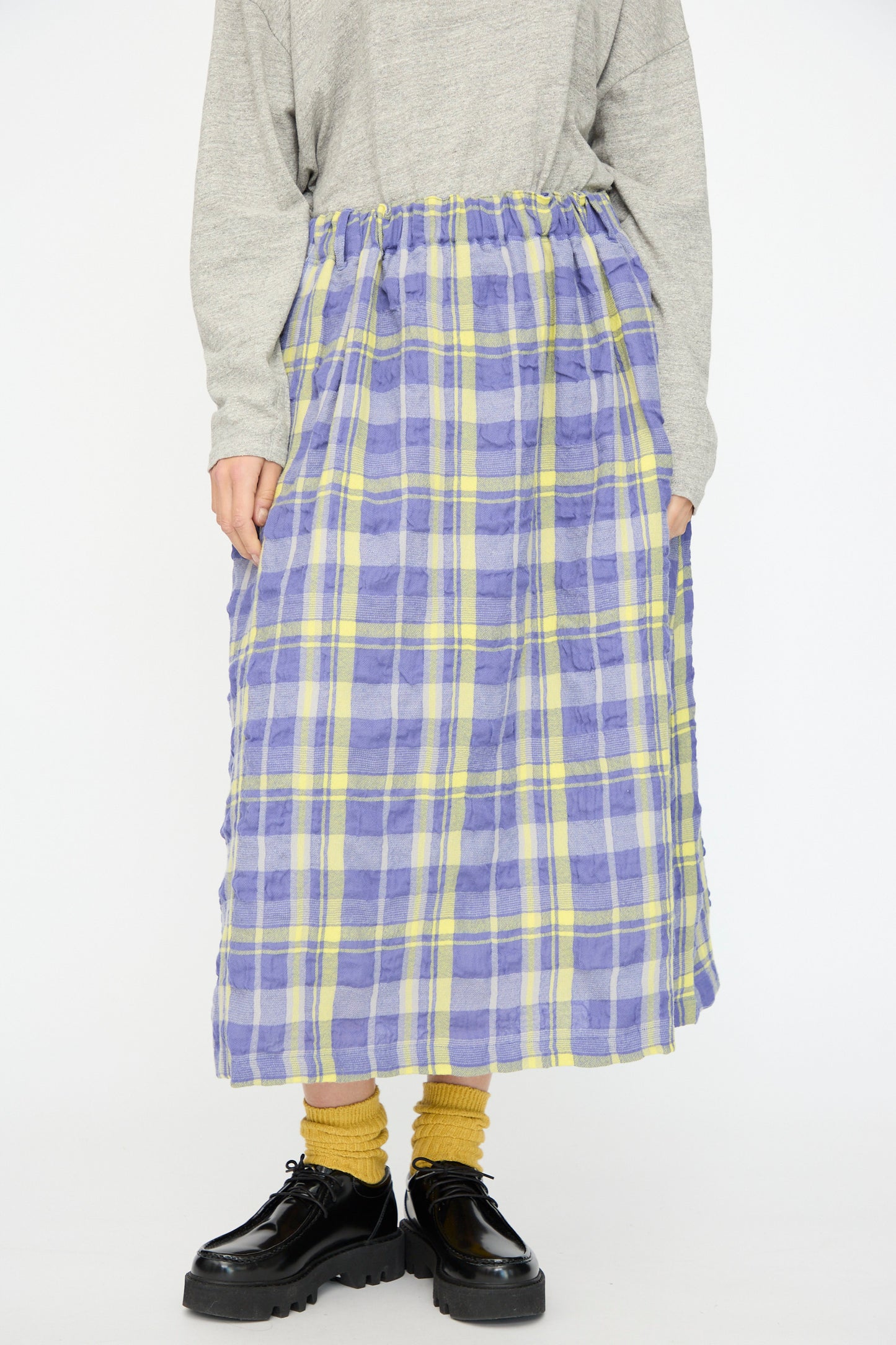 Someone stands against a plain background wearing a gray long-sleeve top, yellow socks, black shoes, and the Ichi Antiquités Cotton Wool Tartan Check Skirt in Blue, featuring an elastic waist and blue-and-yellow plaid pattern.