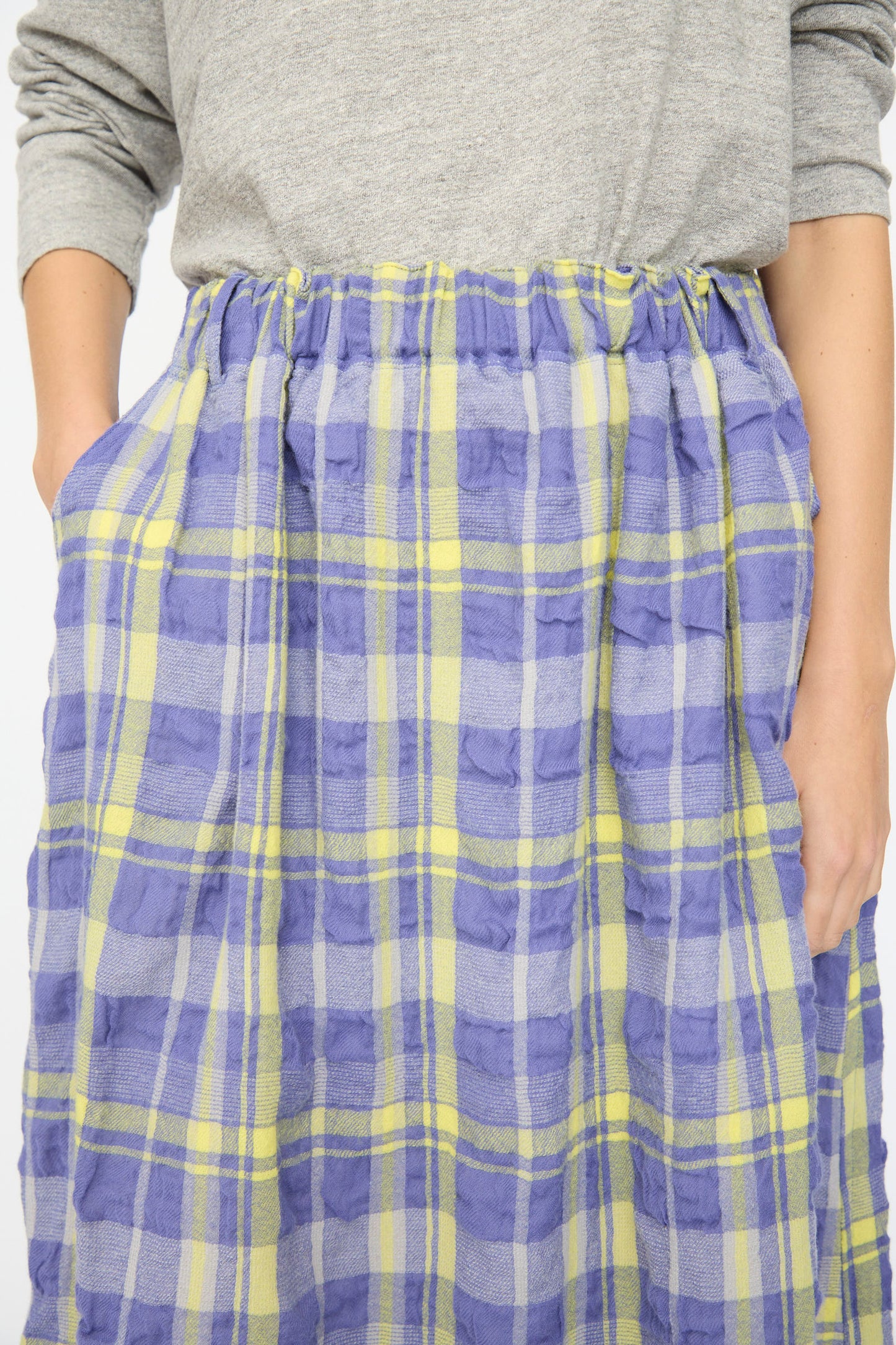 A person in a gray long-sleeve shirt and the Ichi Antiquités Cotton Wool Tartan Check Skirt in Blue, hands in the skirt's pockets.
