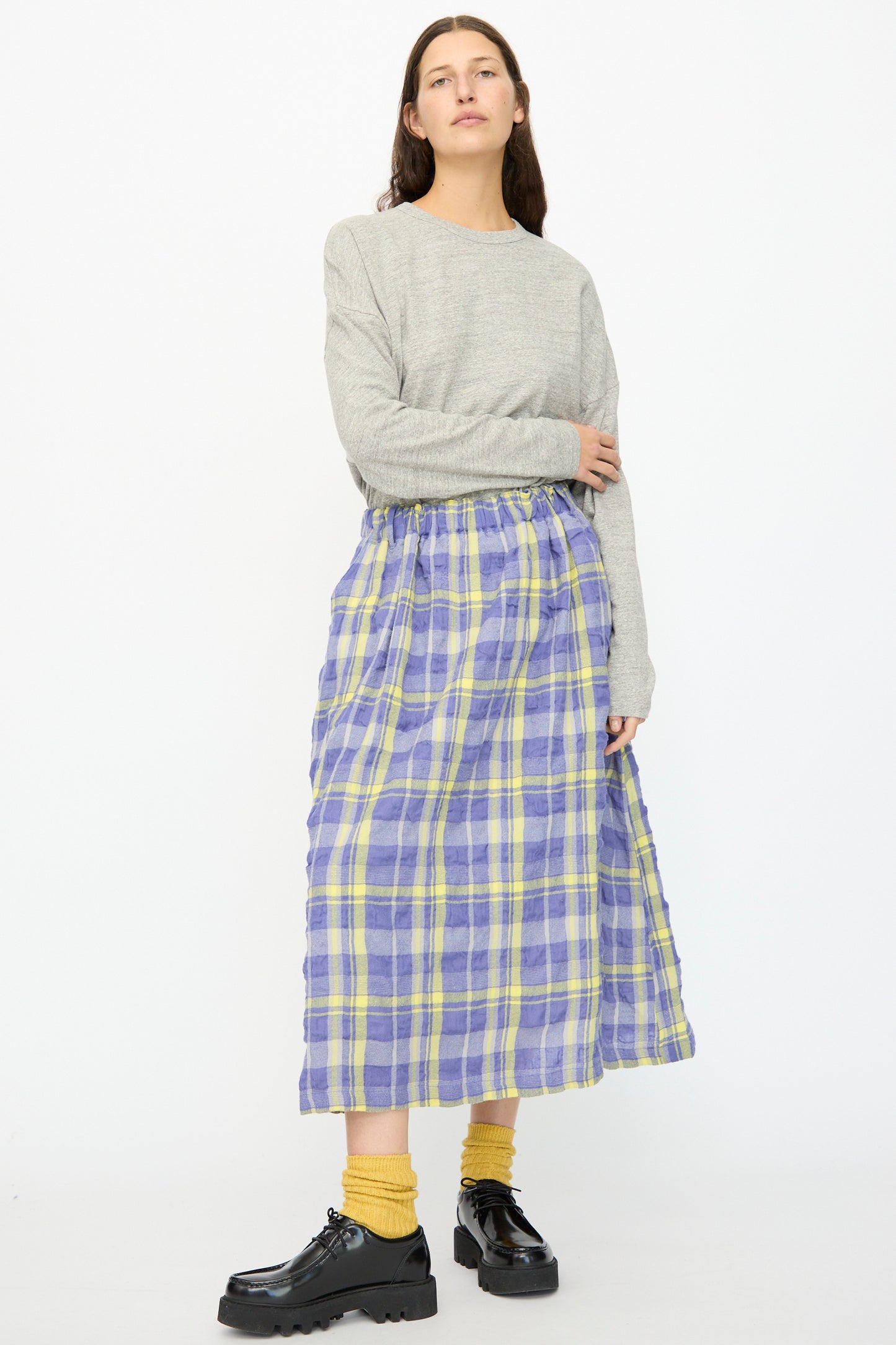 A person stands against a white background wearing a grey long-sleeve top, yellow socks, black shoes, and the Ichi Antiquités Cotton Wool Tartan Check Skirt in Blue.