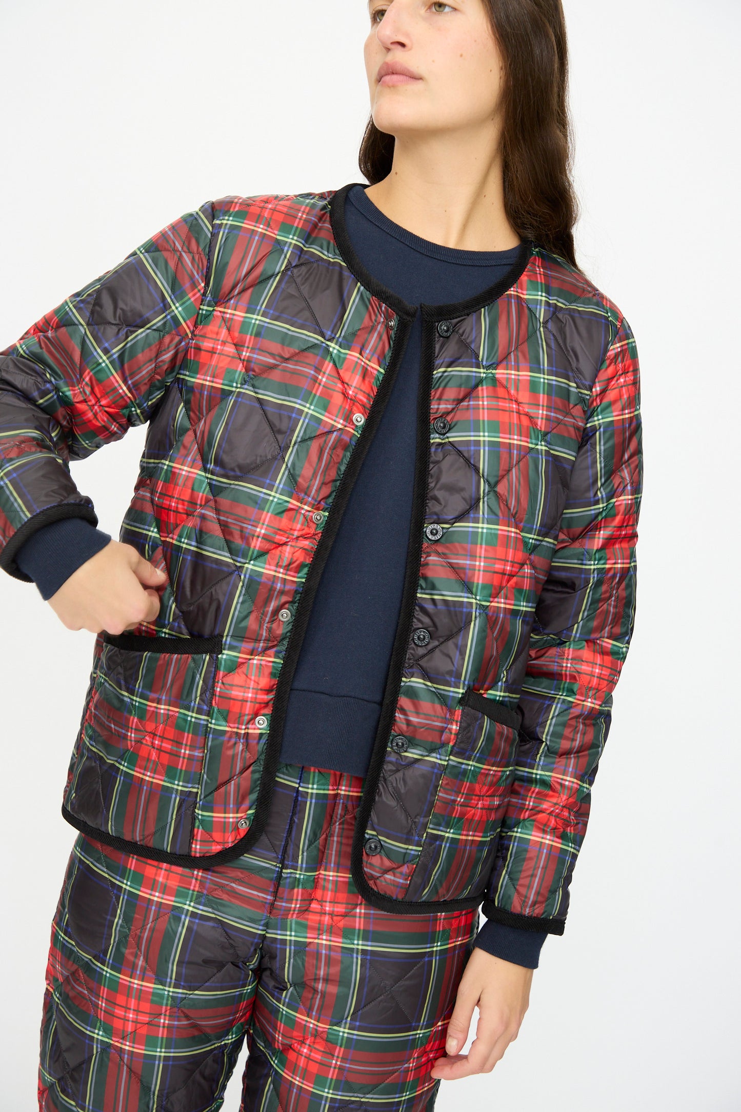 Person wears the Ichi Antiquités Down Jacket in Black Tartan, featuring black corduroy trim, with matching pants and a navy blue shirt, standing against a plain white background.