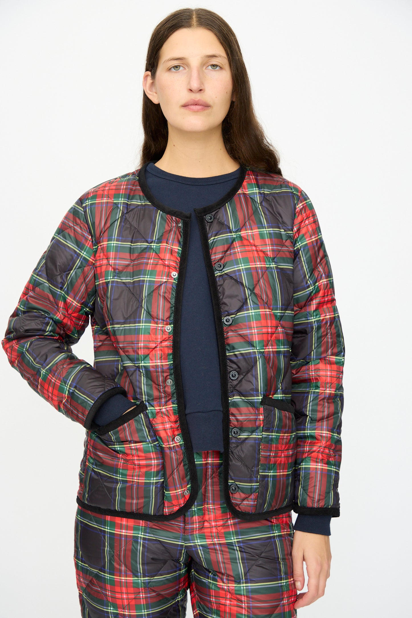 A person models the Ichi Antiquités Down Jacket in Black Tartan, featuring a matching plaid design with black corduroy trim, against a plain white background.