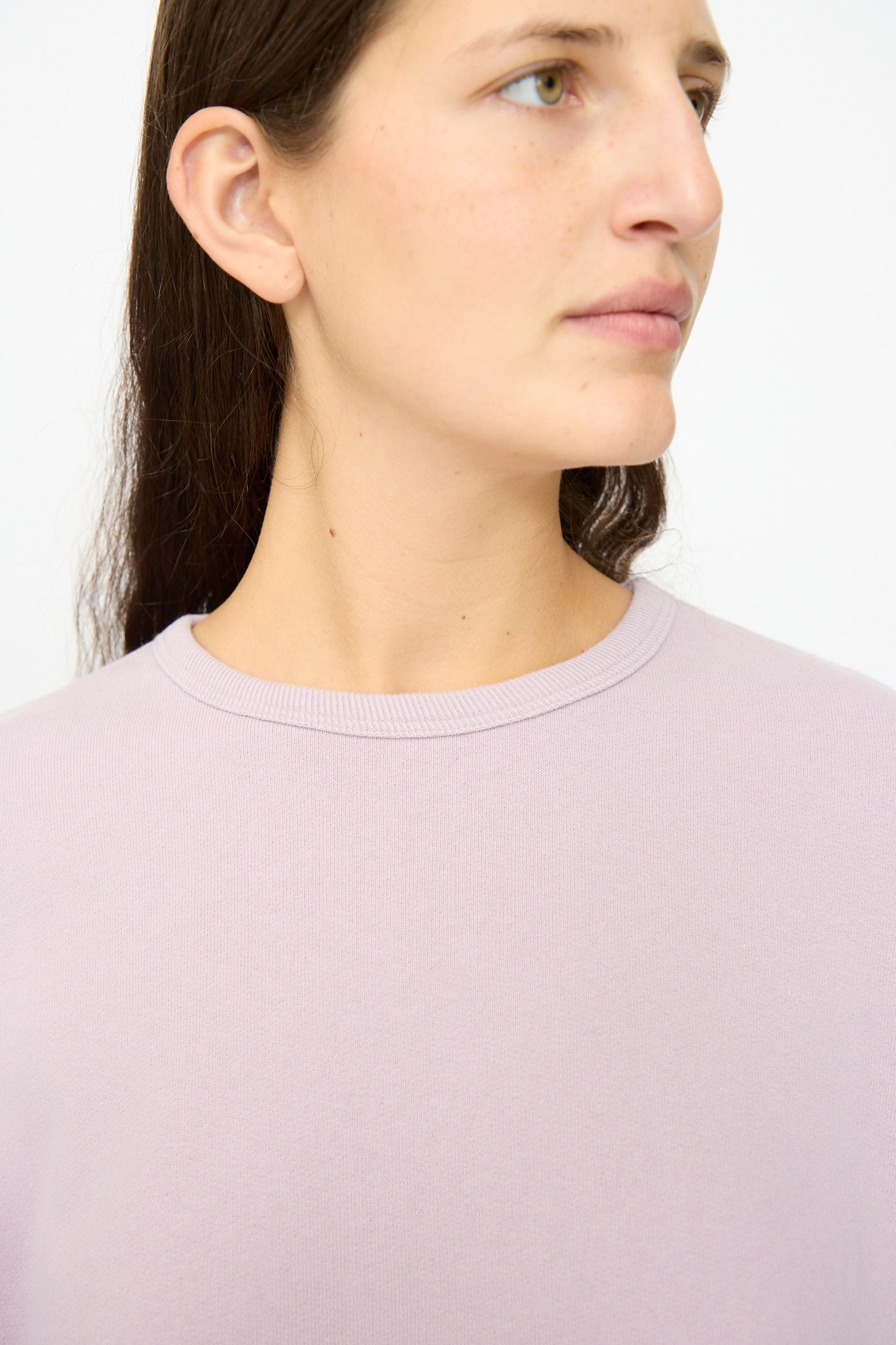 A woman with long brown hair is shown from the shoulders up, looking slightly right, wearing the Ichi Antiquités French Terry Cotton Pullover in Lavender.