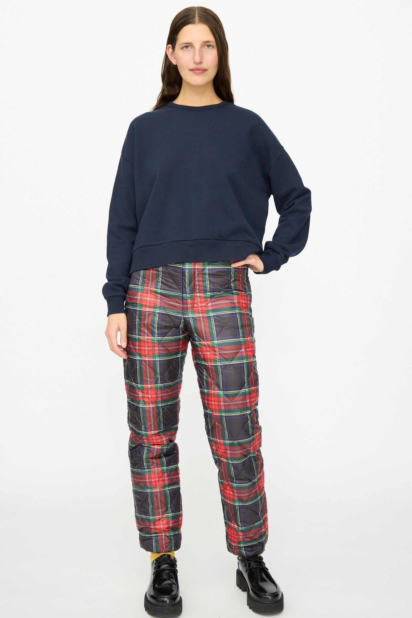 A woman faces forward against a plain white background, wearing the Ichi Antiquités French Terry Cotton Pullover in Navy, paired with plaid quilted pants and black platform shoes.