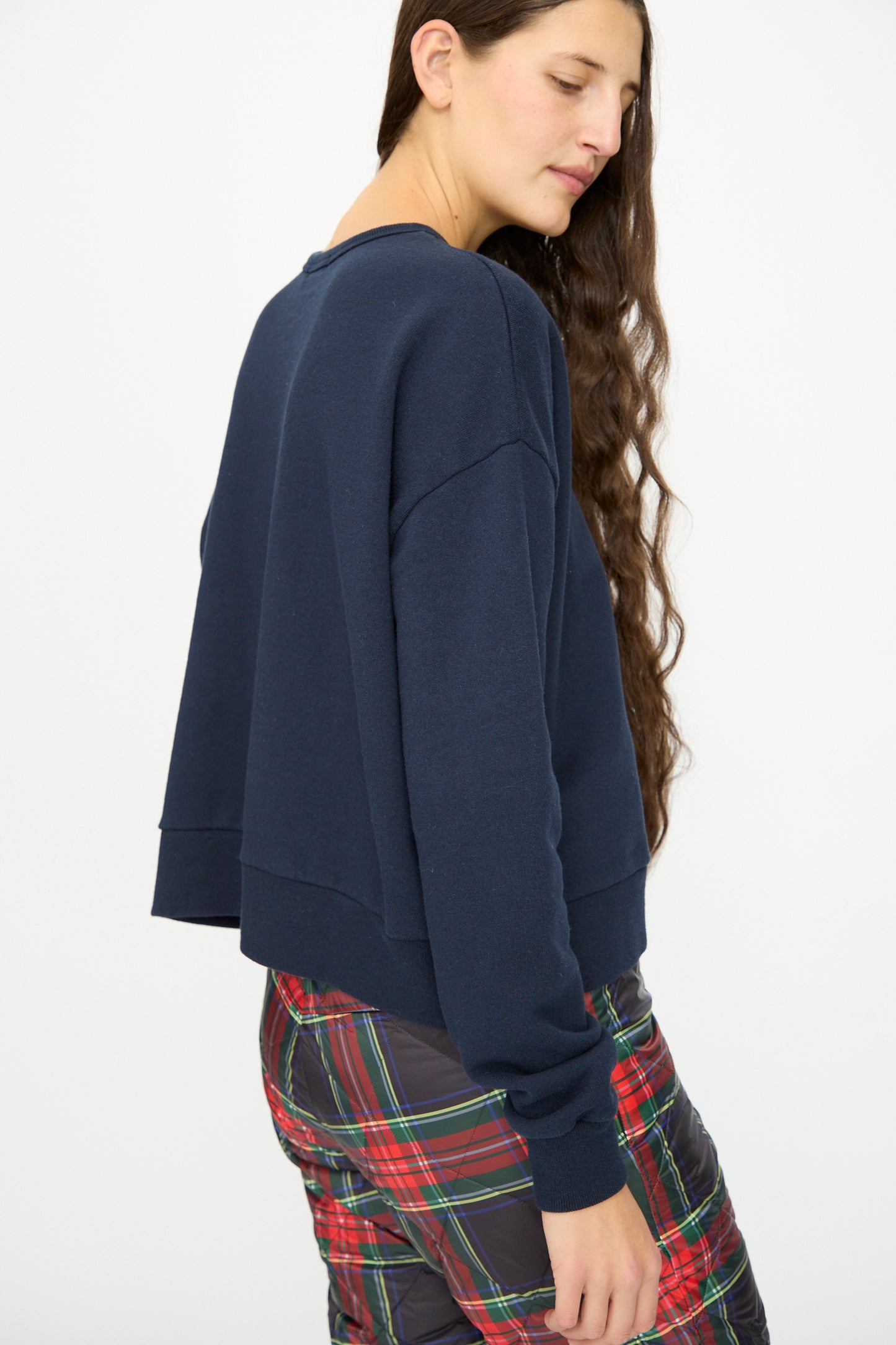 A woman with long brown hair models the Ichi Antiquités French Terry Cotton Pullover in Navy and plaid pants, standing sideways against a plain white background.