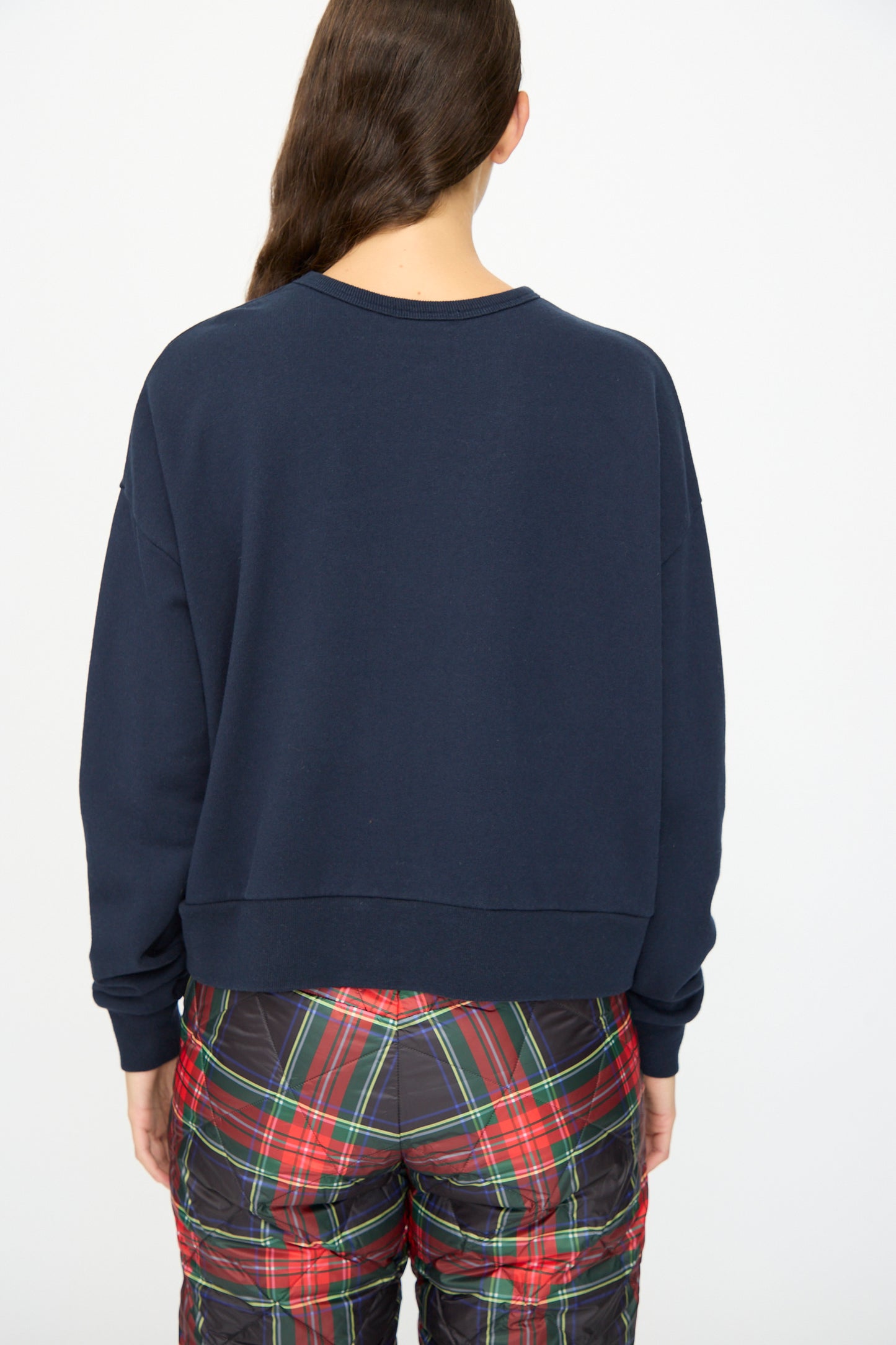 A person faces away, wearing the Ichi Antiquités French Terry Cotton Pullover in Navy and red plaid pants, with long dark hair over one shoulder.