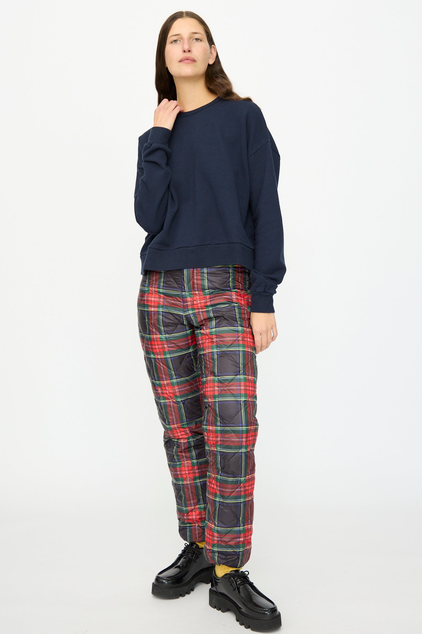 A person stands against a white background wearing the Ichi Antiquités French Terry Cotton Pullover in Navy, red plaid pants, and black platform shoes.