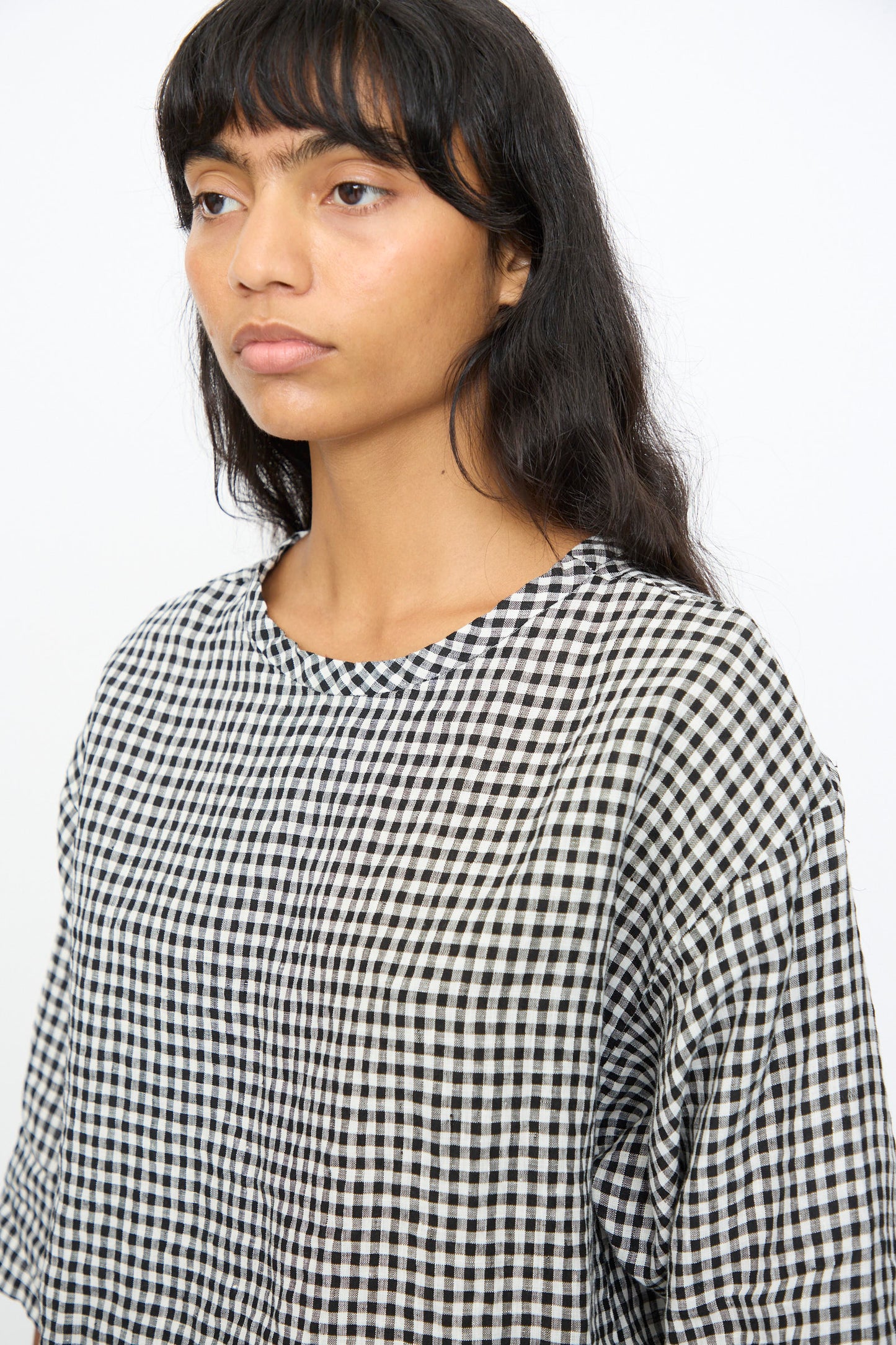 A person with long dark hair and bangs wears the Ichi Antiquités Gingham Check Blouse in White and Black, featuring an oversized fit, while looking slightly to the side against a plain white background.