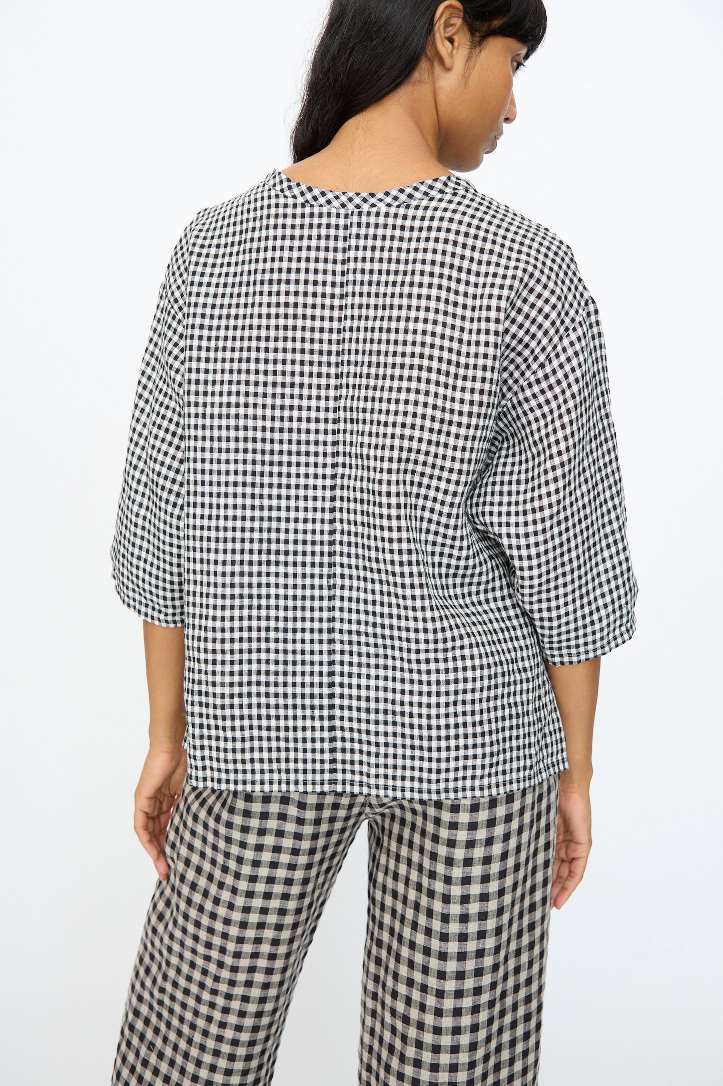A person stands facing away, wearing the Ichi Antiquités Gingham Check Blouse in White and Black with three-quarter sleeves, paired with matching checkered pants, both made in Japan.